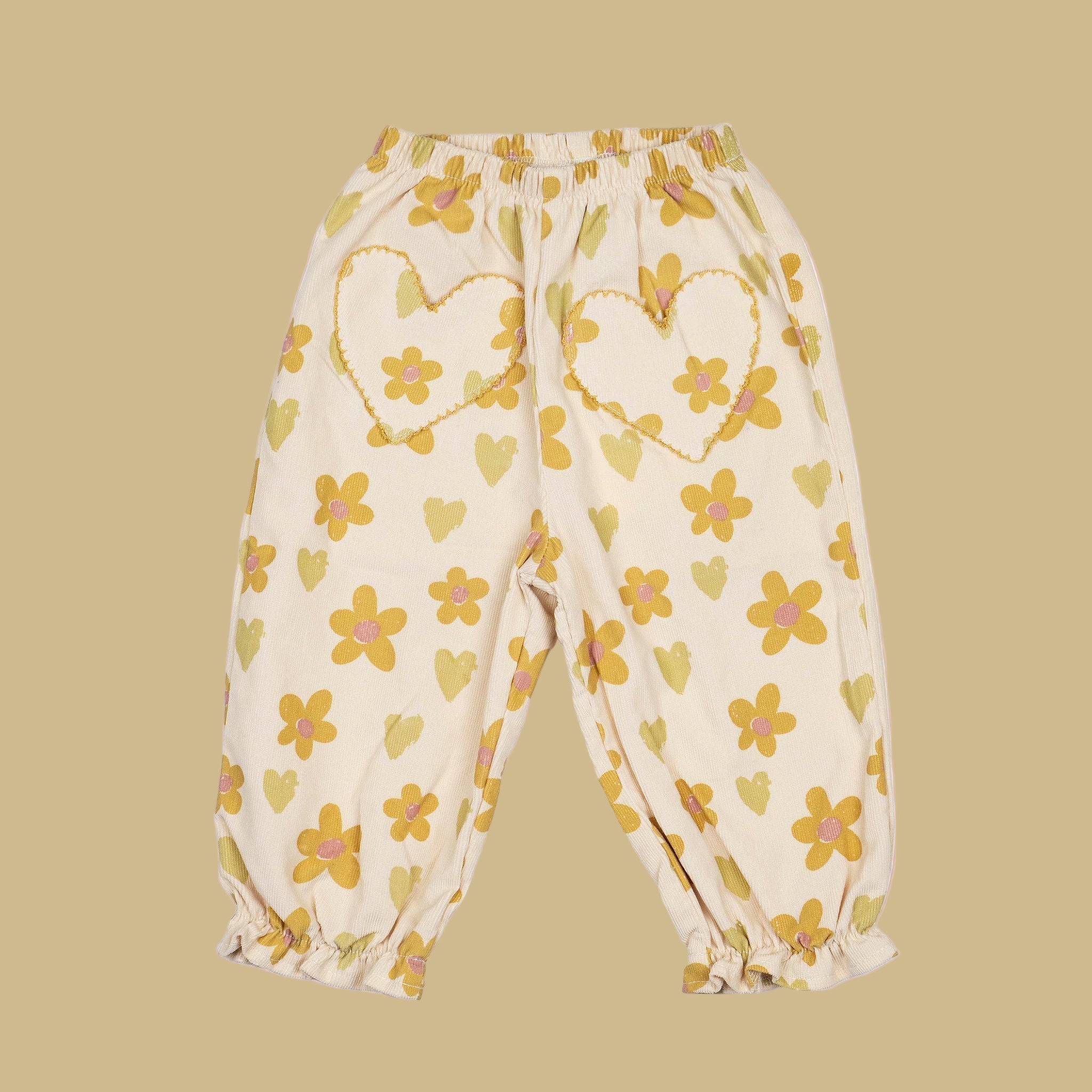 A pair of neutral kids pants with yellow and green floral and heart prints with heart shaped pockets. 