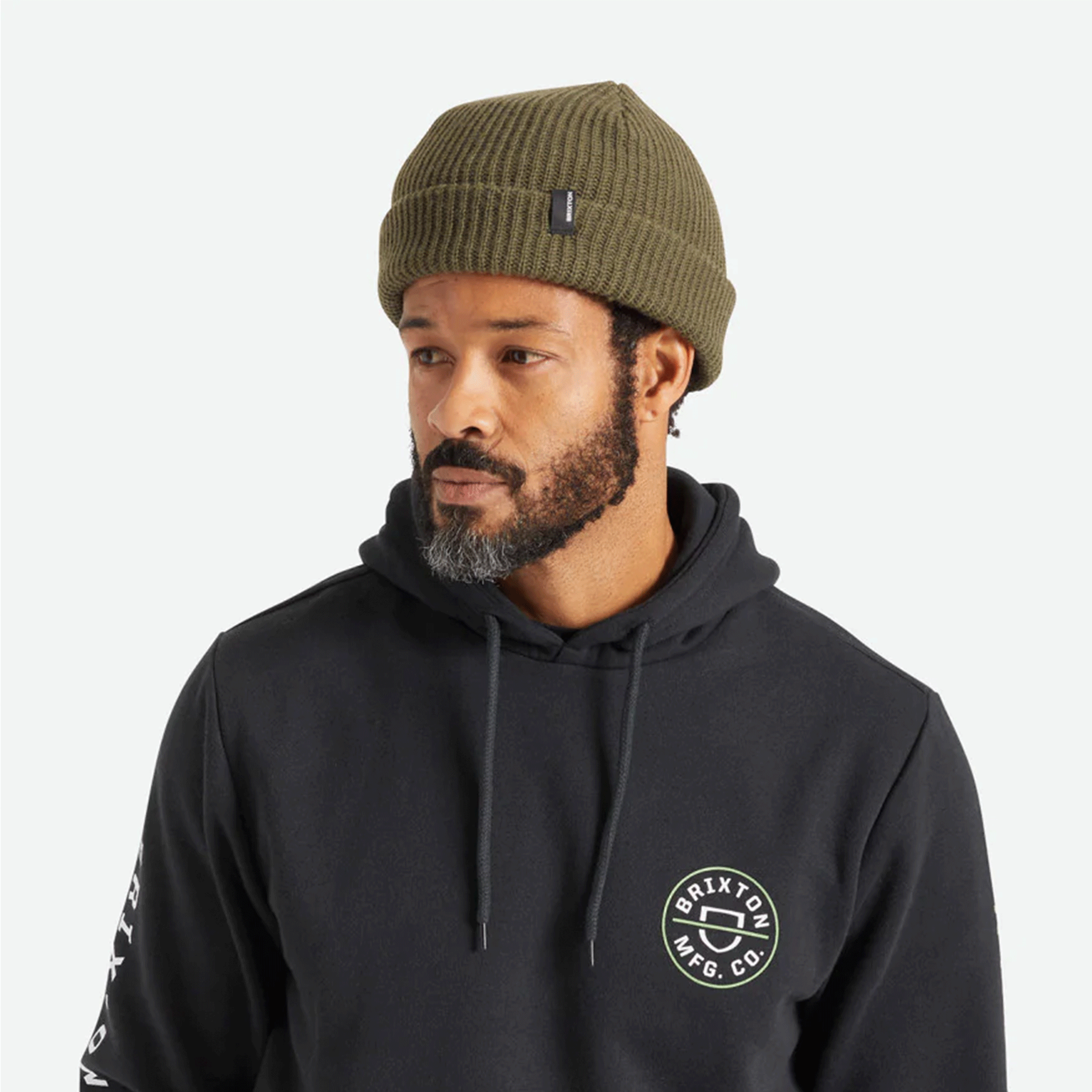 An olive green knit beanie with plush acrylic and has a folding cuff detailed with a woven label.