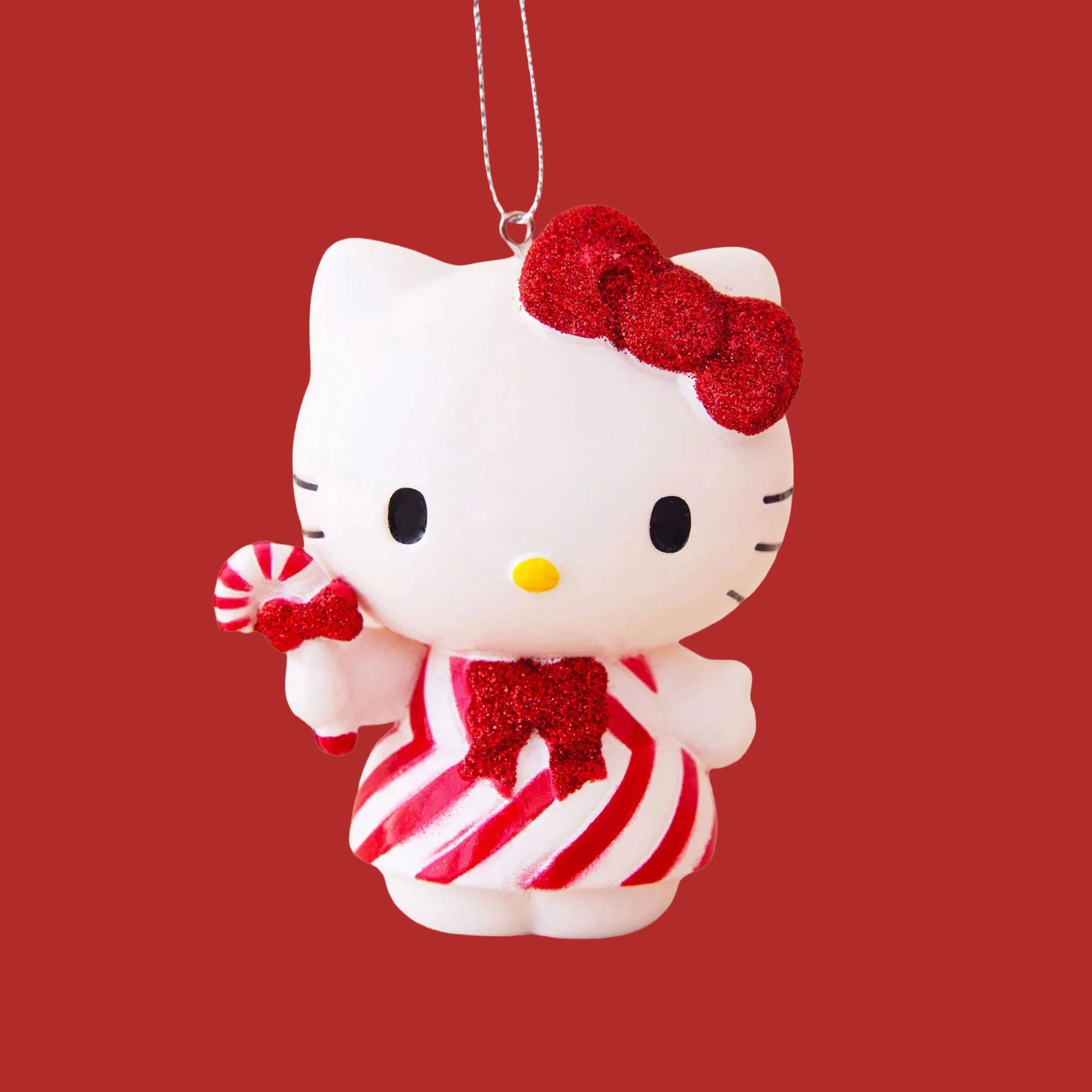 A white and red Hello Kitty ornament holding a candy cane and wearing a striped dress. 