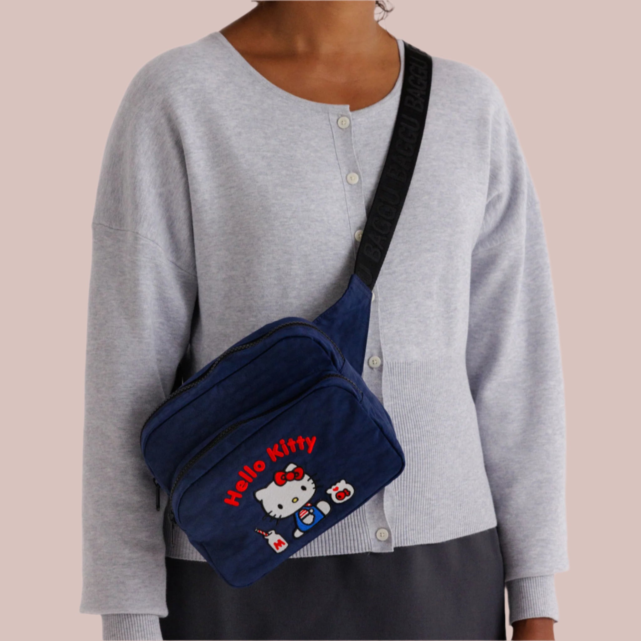 A navy blue nylon fanny pack with a black strap and an embroidered Hello Kitty milkshake design with red text that reads, &#39;Hello Kitty&#39;. 
