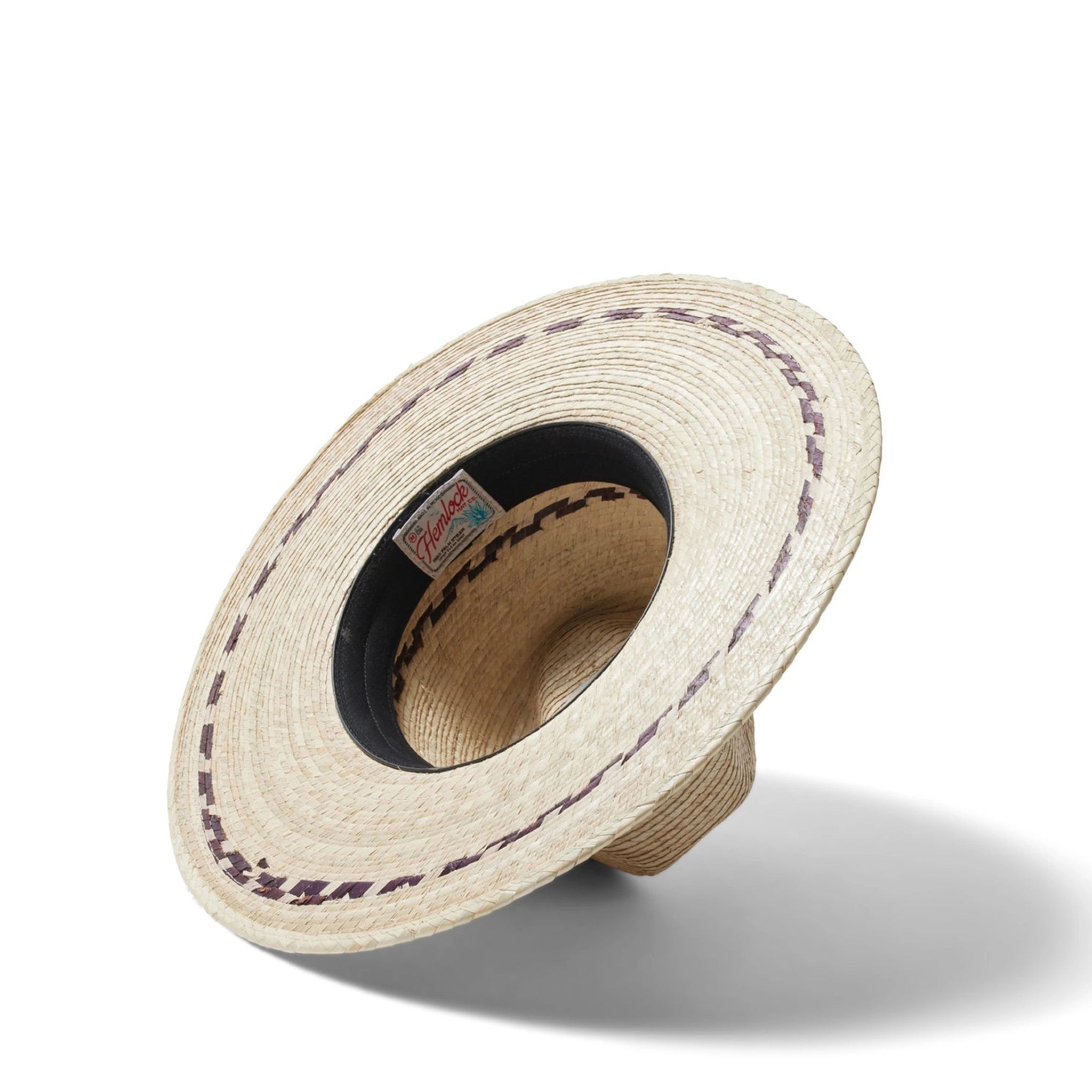 On a neutral background is a tan woven sun hat with a wide brim and brown stitching details around the bottom of the brim as well as around the base of the hat.