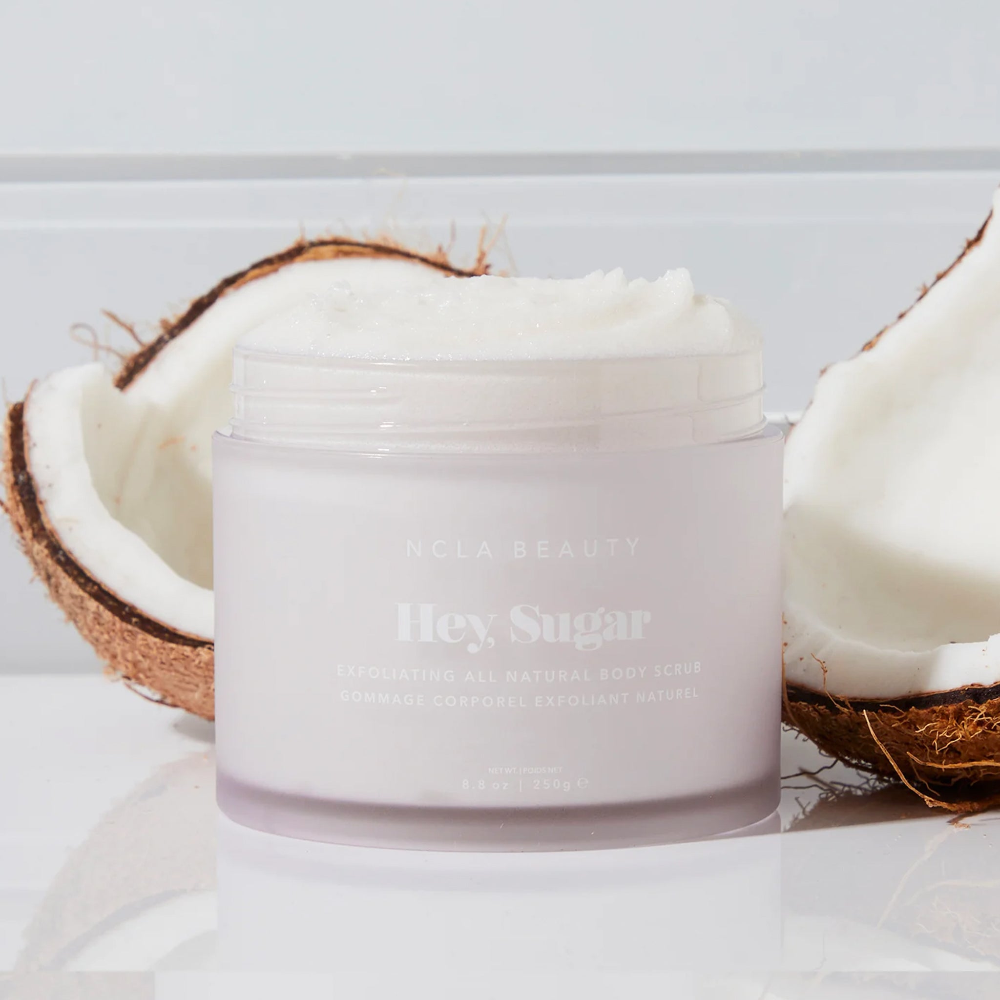 On a tiled  background is a container of white colored body scrub with text on the front that reads, "Hey, Sugar".