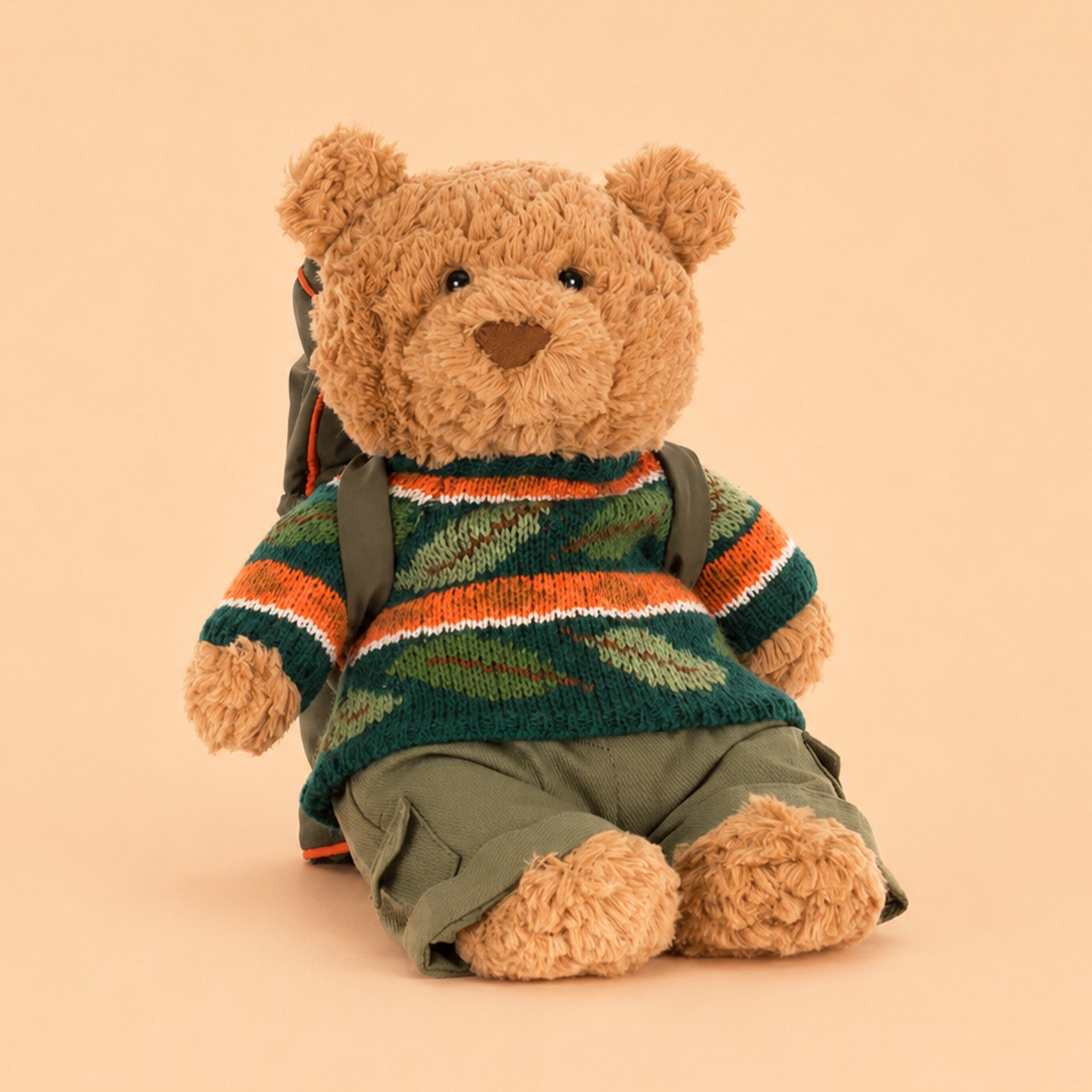 Teddy bear wearing a striped sweater and backpack on a beige background