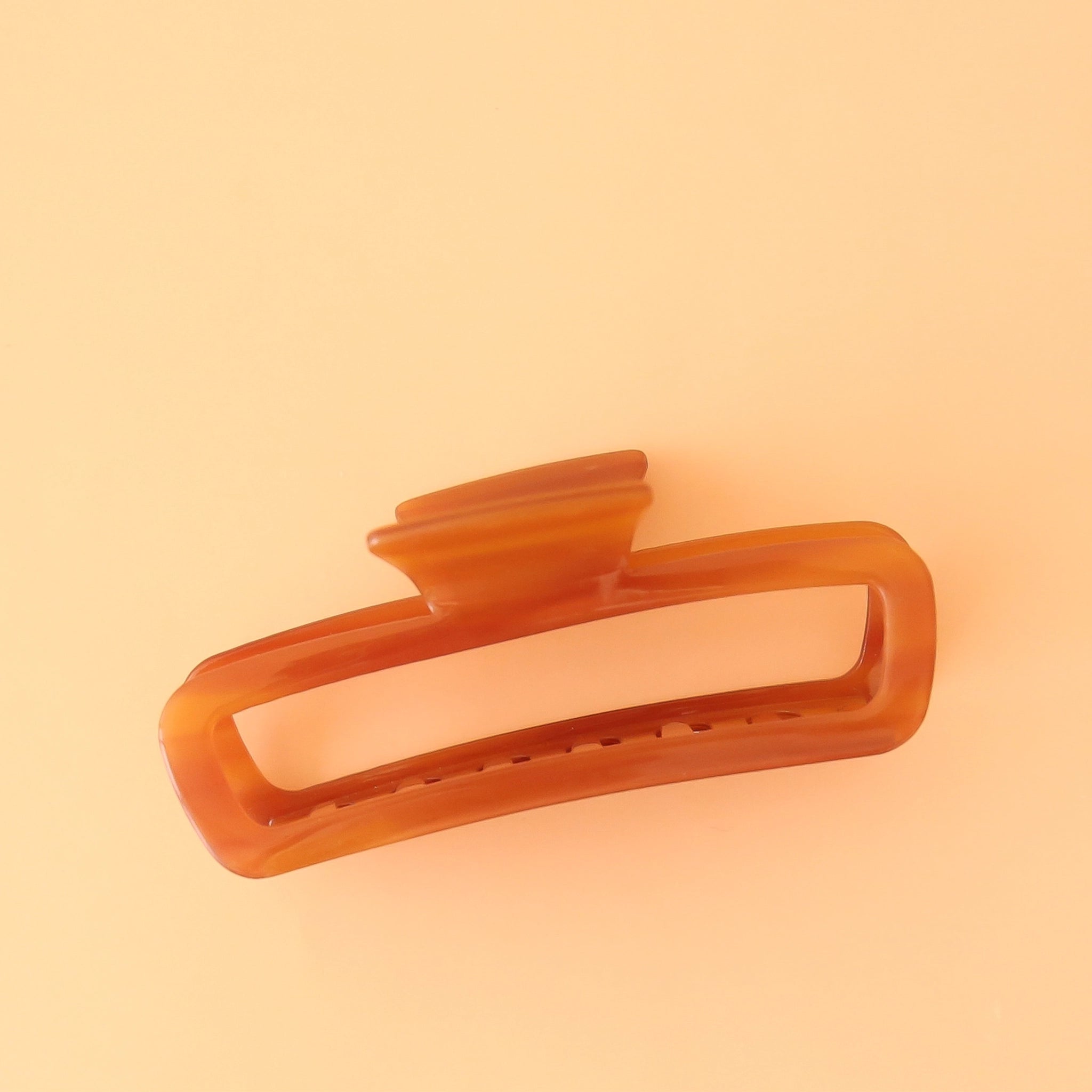 On a peachy background is an amber colored rectangle claw clip with slightly rounded edges.