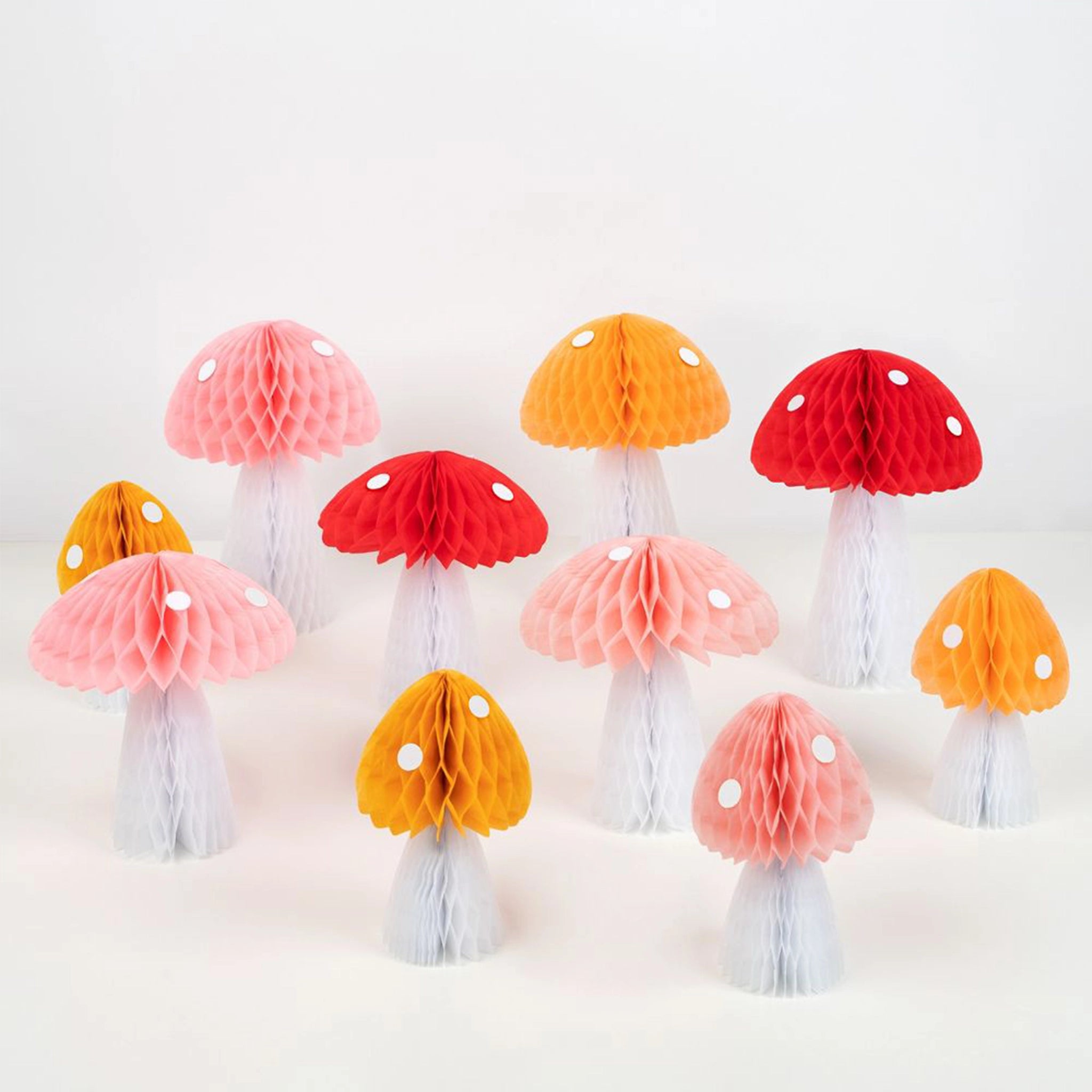 A variety of honeycomb mushroom decorations on a tablescape. There are pink, red and yellow mushrooms with white dots.