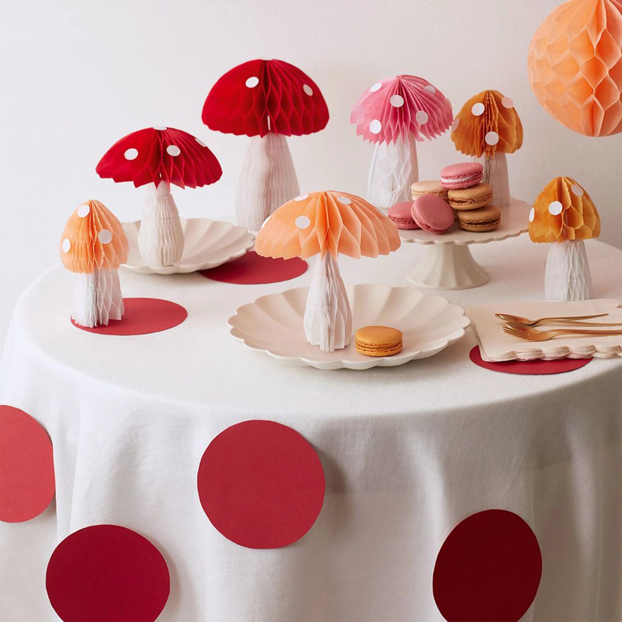 A variety of honeycomb mushroom decorations on a tablescape. There are pink, red and yellow mushrooms with white dots. 