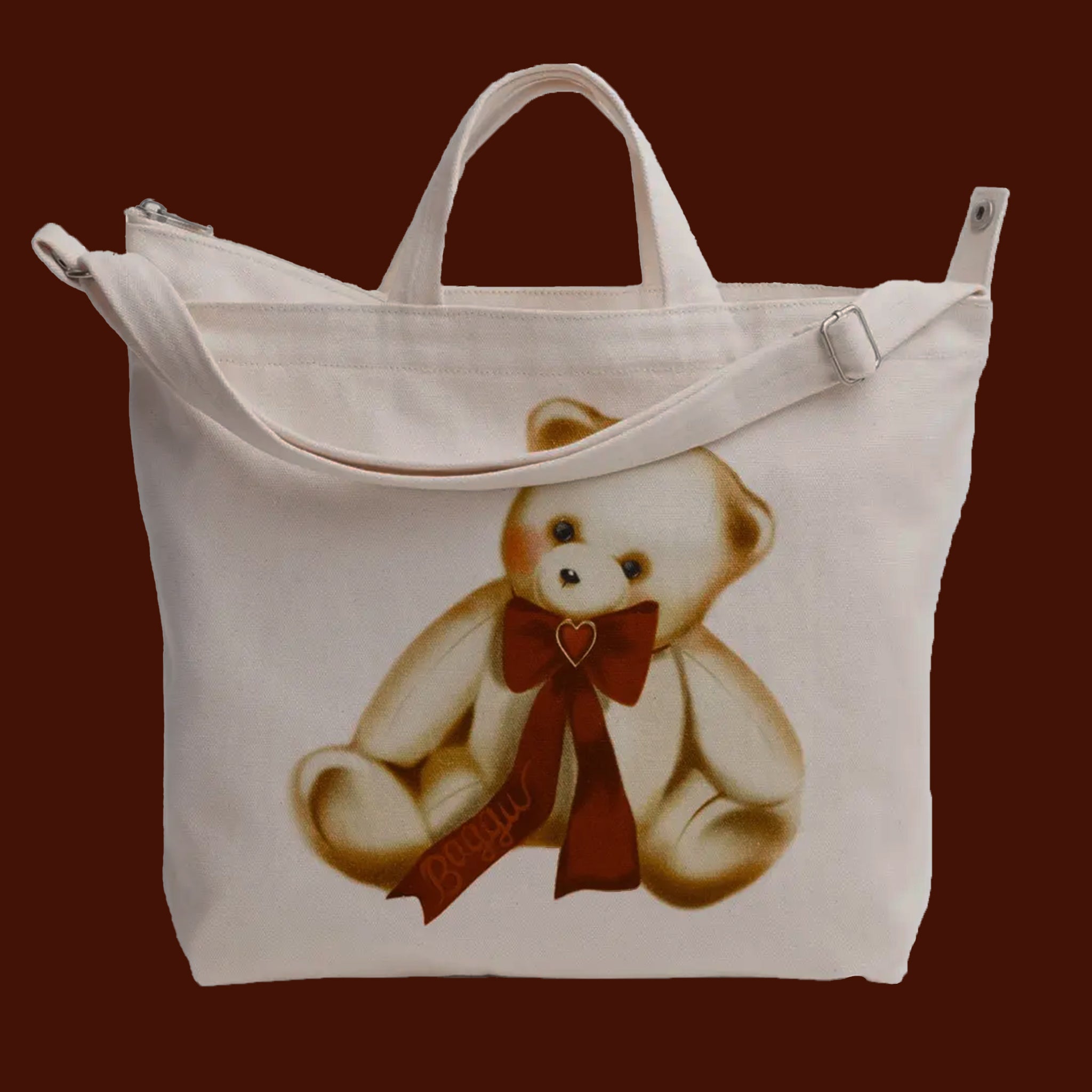 An ivory canvas bag with a shoulder strap and short handle and a teddy bear red bow graphic. 