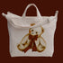 An ivory canvas bag with a shoulder strap and short handle and a teddy bear red bow graphic. 