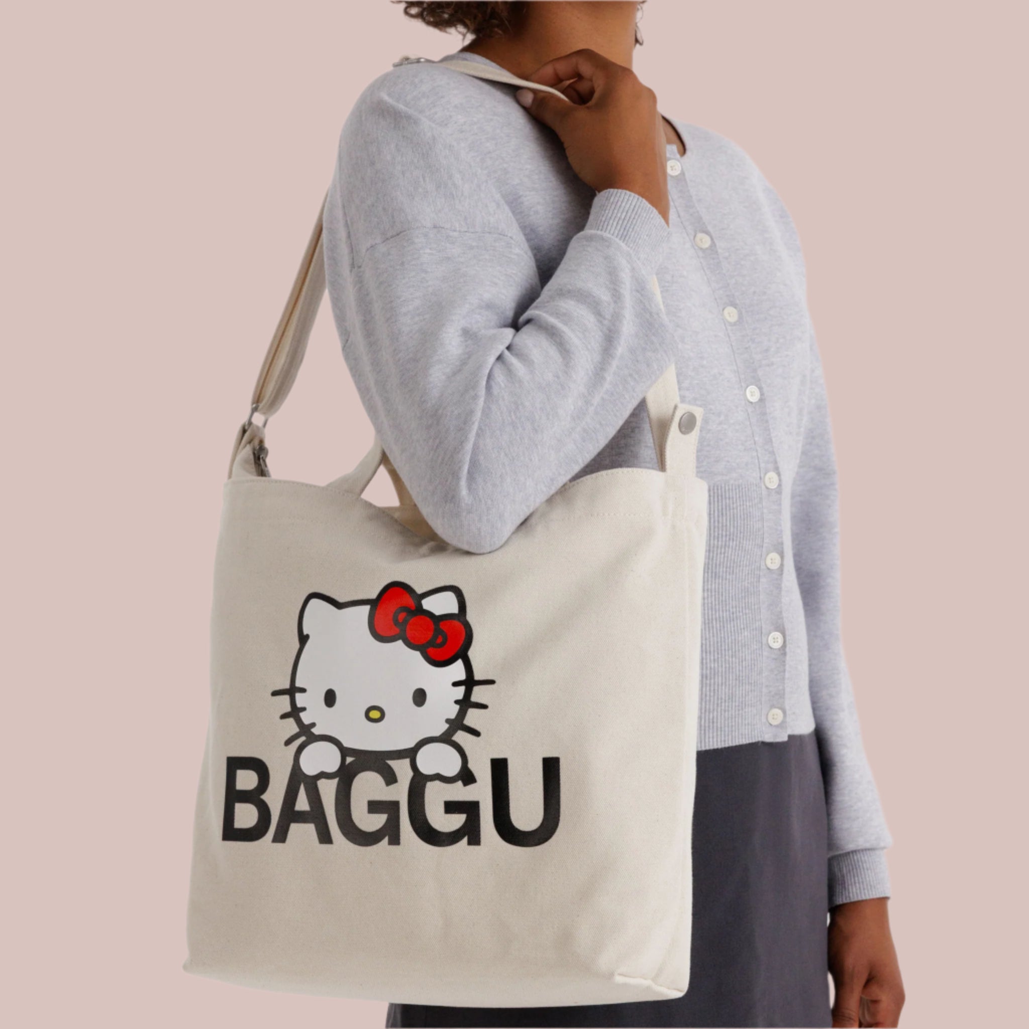 A neutral canvas bag with a shoulder strap and a screen printed Hello Kitty and black BAGGU logo. 
