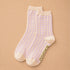 A pair of light cream crew socks with a subtle lavender houndstooth pattern and olive green 'BAGGU' branding printed on the sole, displayed on a warm beige background.