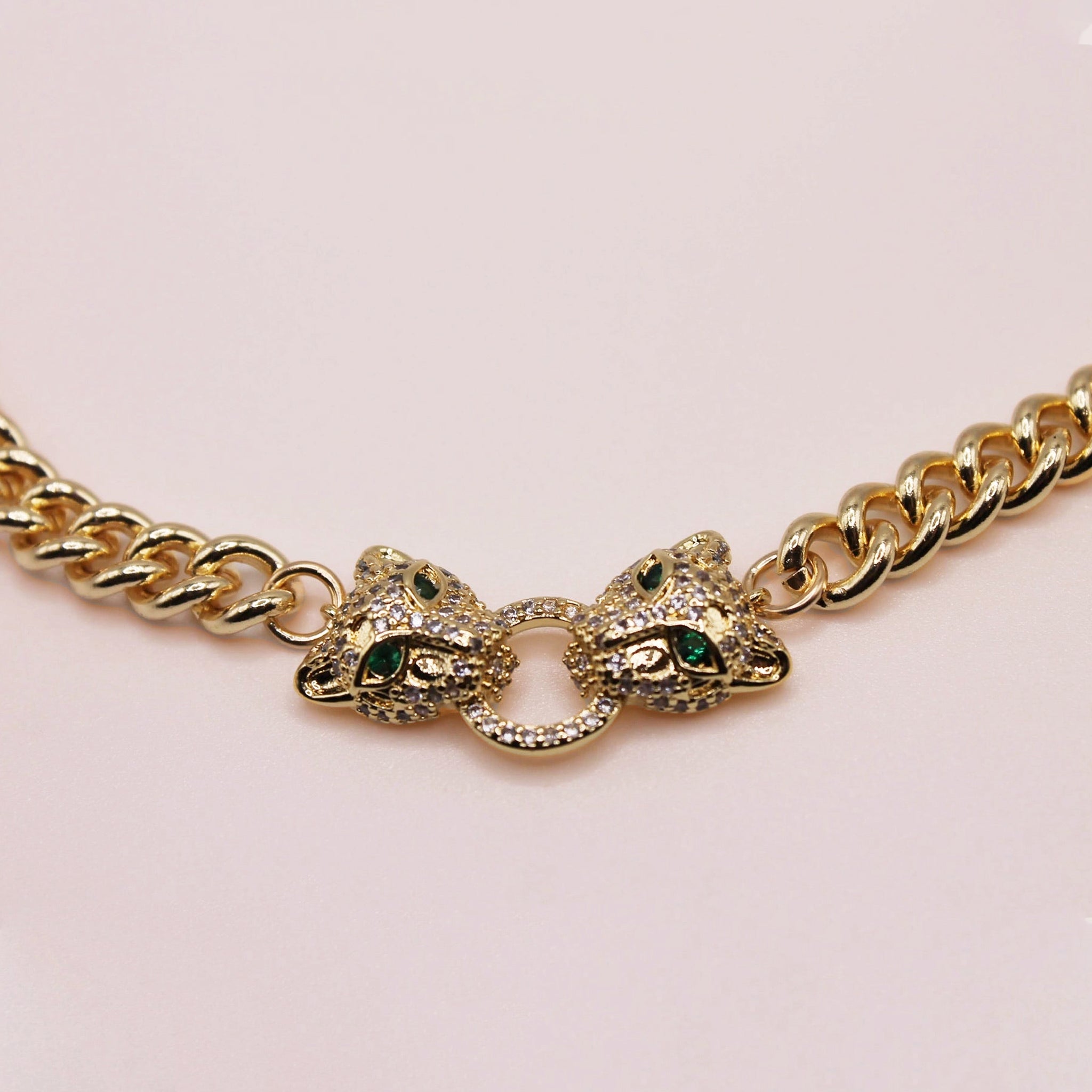 Gold chain bracelet with panther head designs on a light pink background