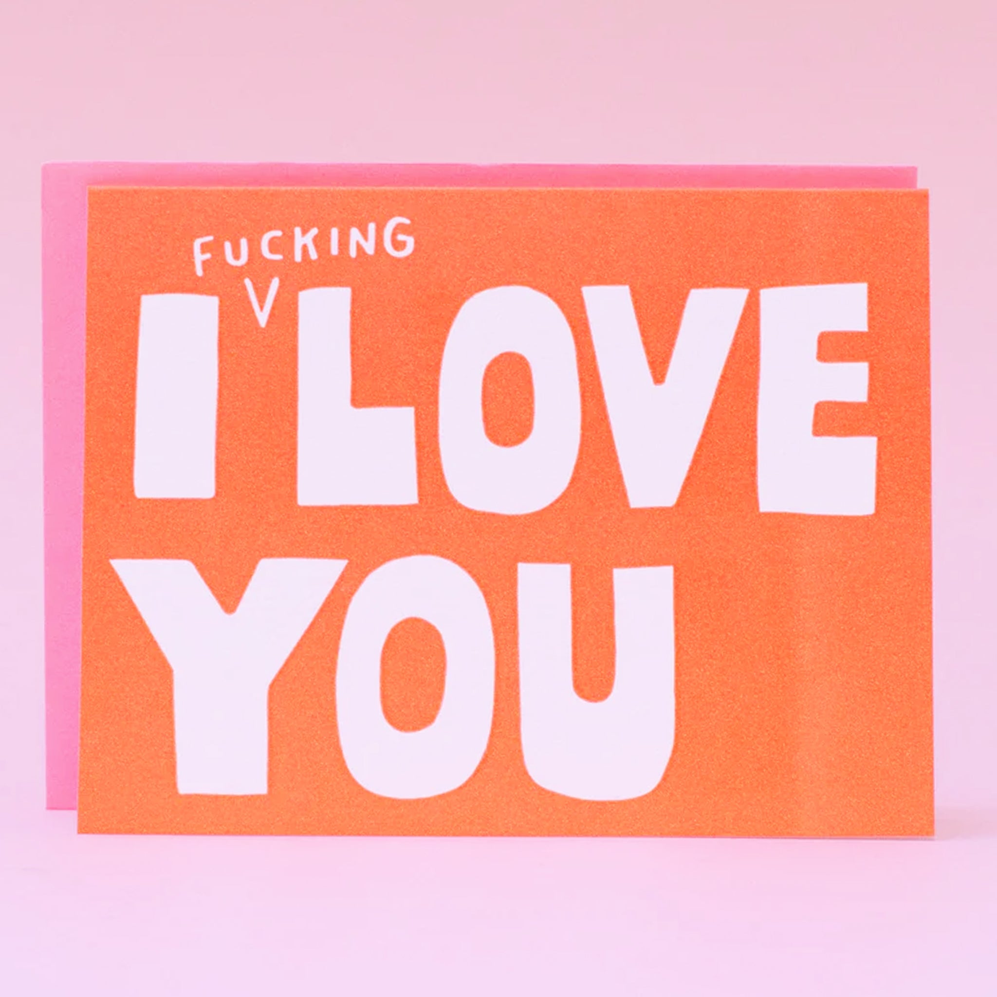 A bright orange card with a pink envelope. The card reads, "I Fucking Love You" in white letters. 