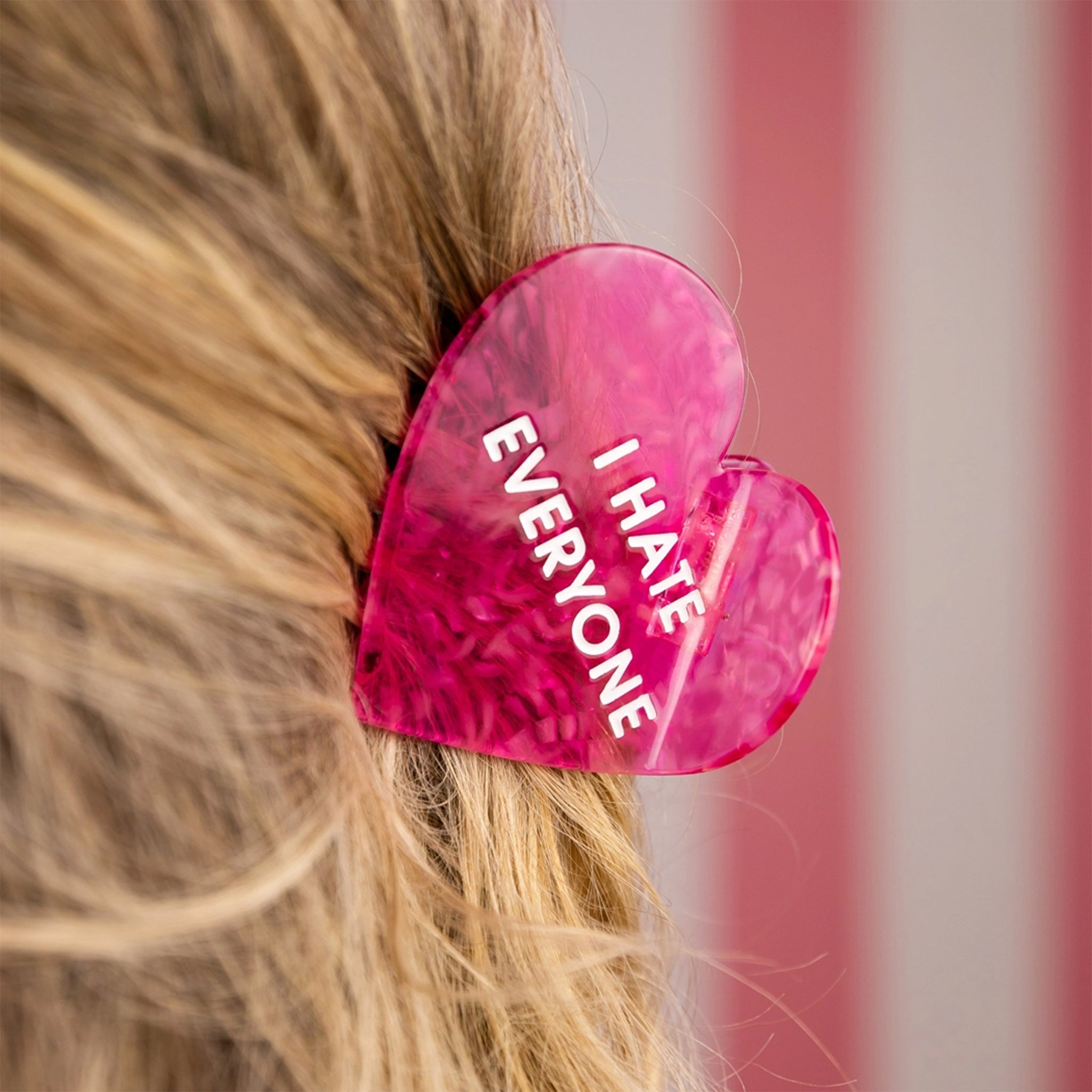 A hot pink heart shaped hair clip with text that reads, "I Hate Everyone". 