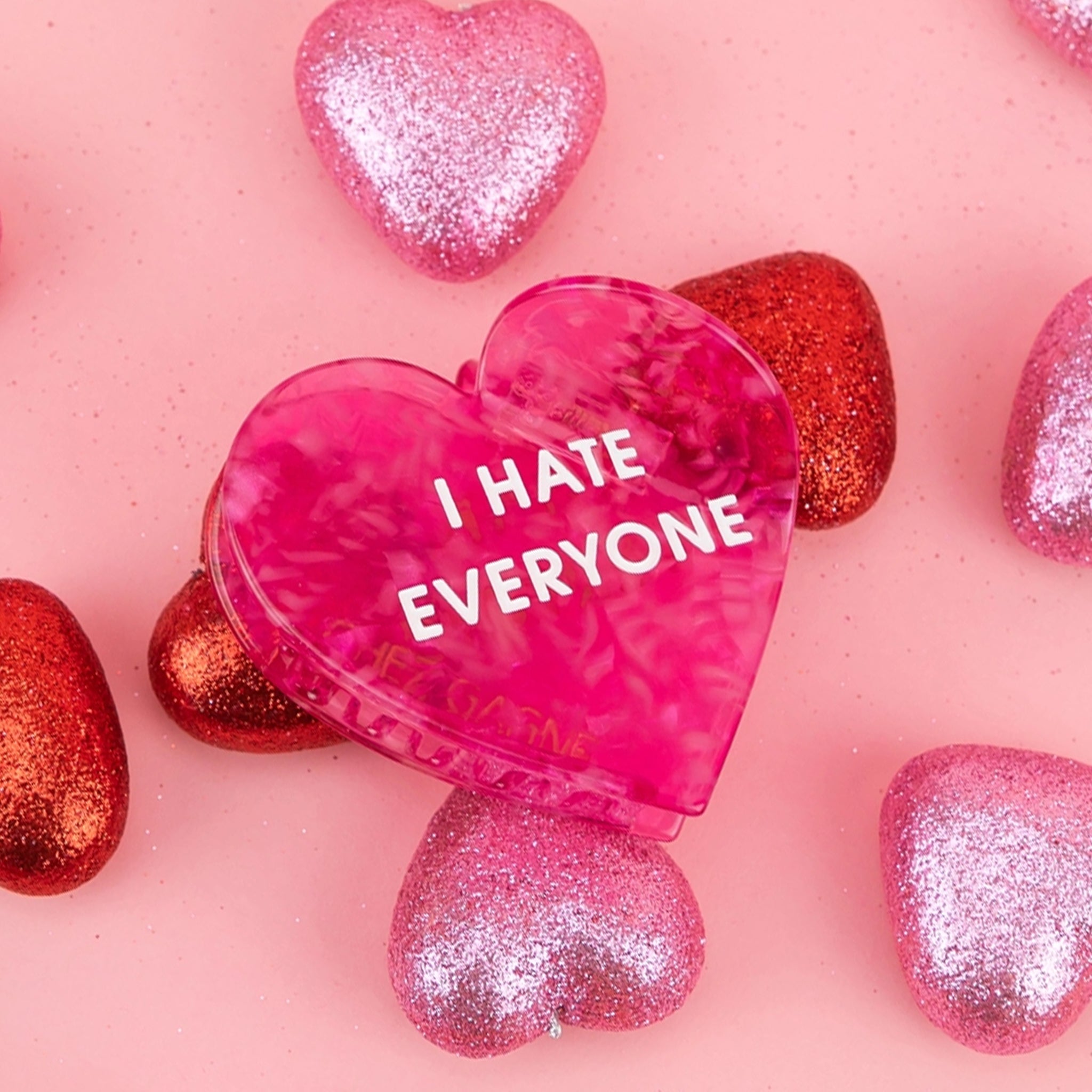 A hot pink heart shaped hair clip with text that reads, "I Hate Everyone". 