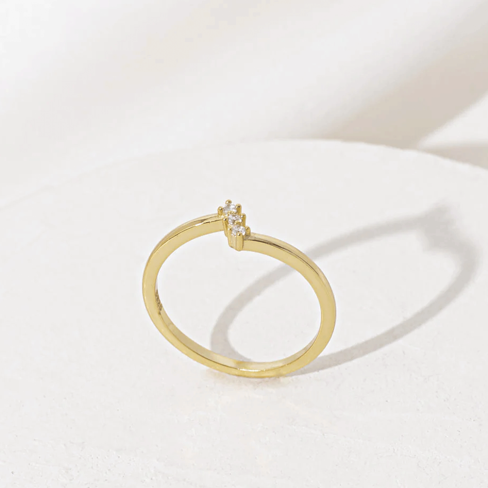The Imagine Ring that is a thin gold band with three cubic zirconia stones stacked on top of one another.
