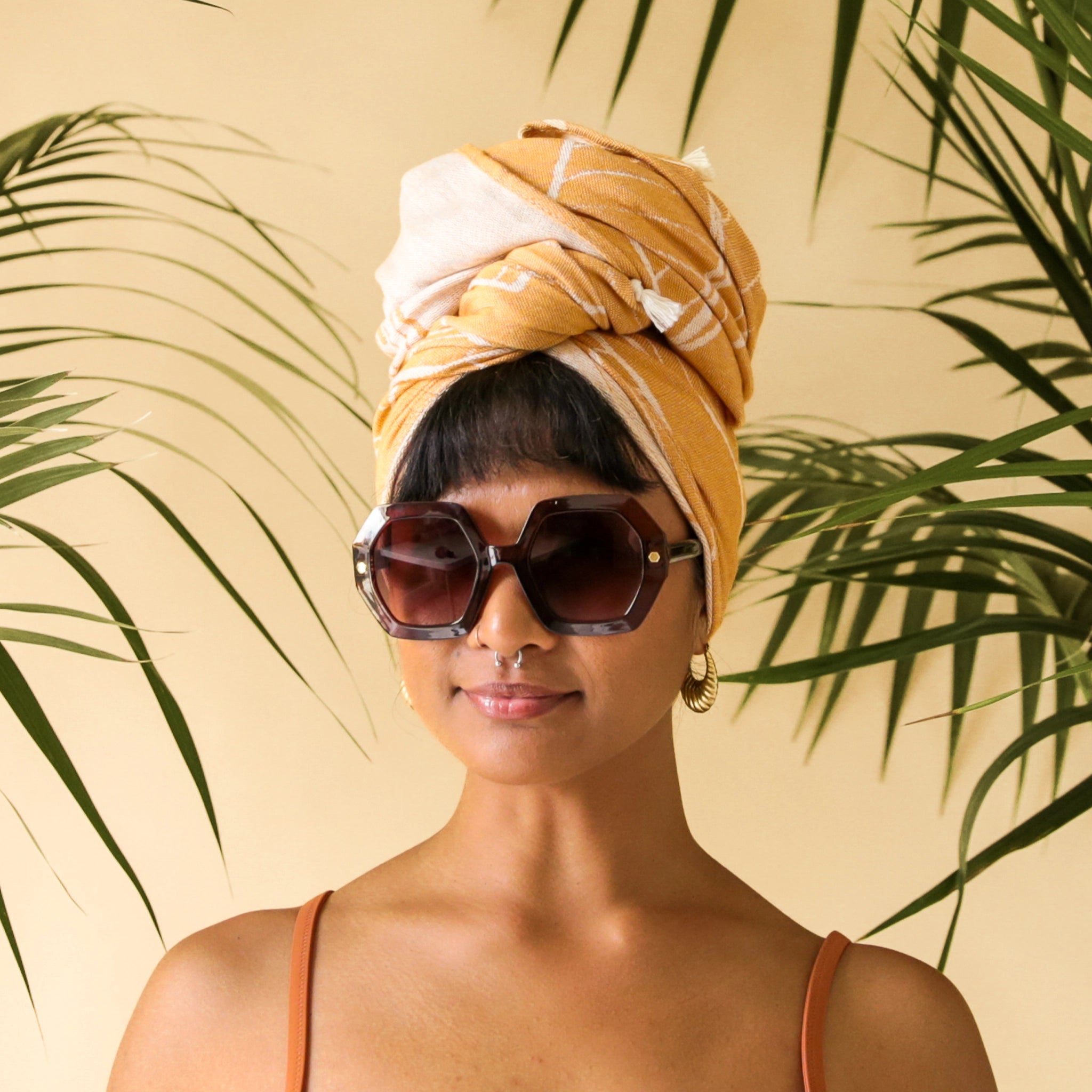 On a peachy background is modeling wearing a pair of hexagon shaped tortoise sunglasses with brown lenses.