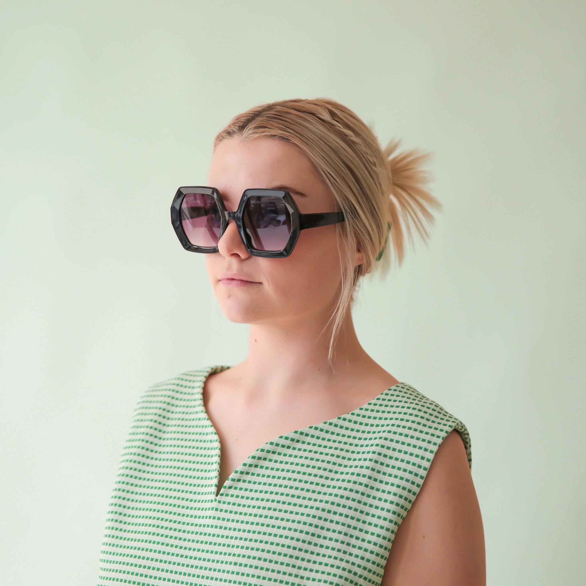 On a mint green background is a model wearing the Iris sunglasses in the shade black.
