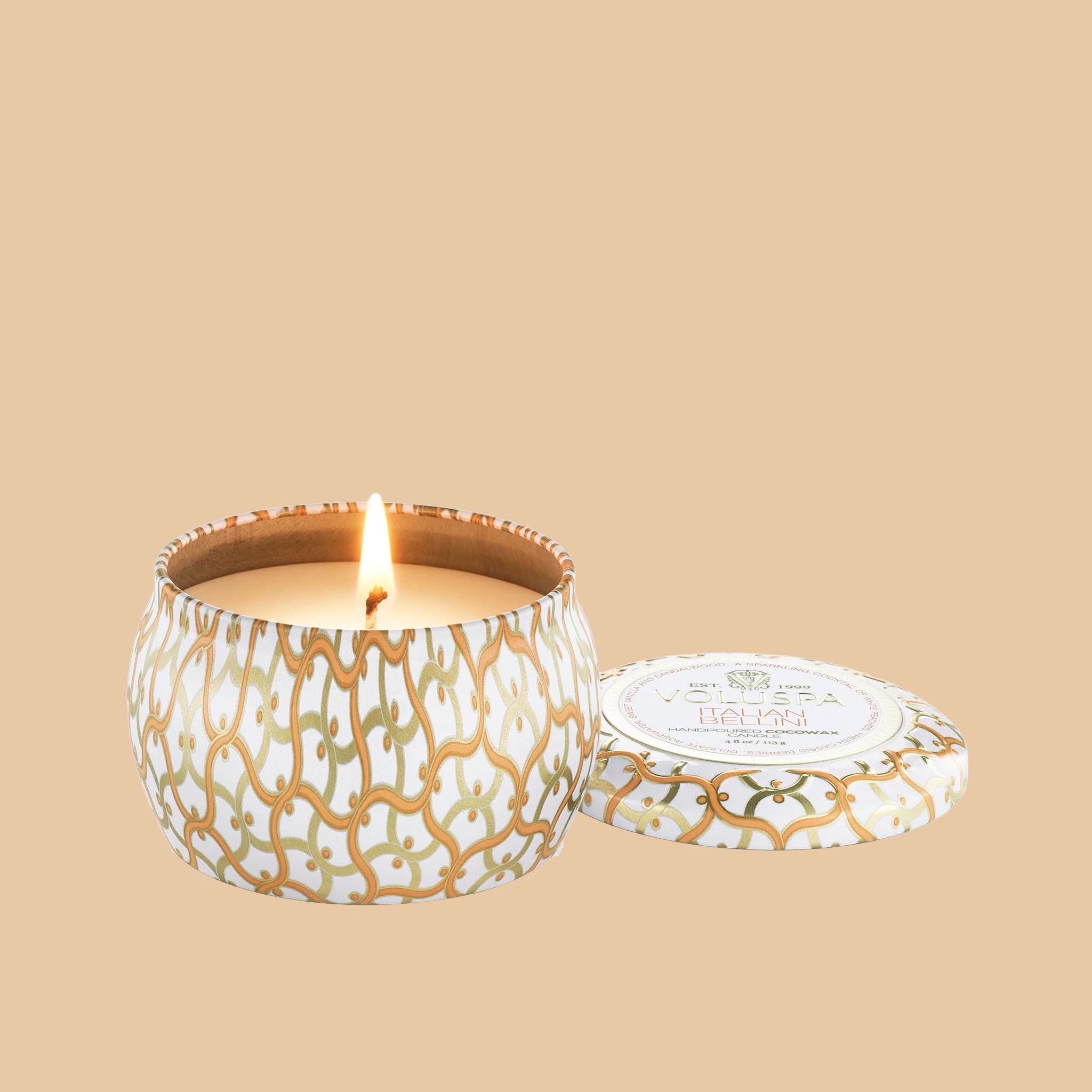 An orange and white tin that contains a single wick candle along with a circle label in the center of the lid that reads, "Voluspa Italian Bellini".