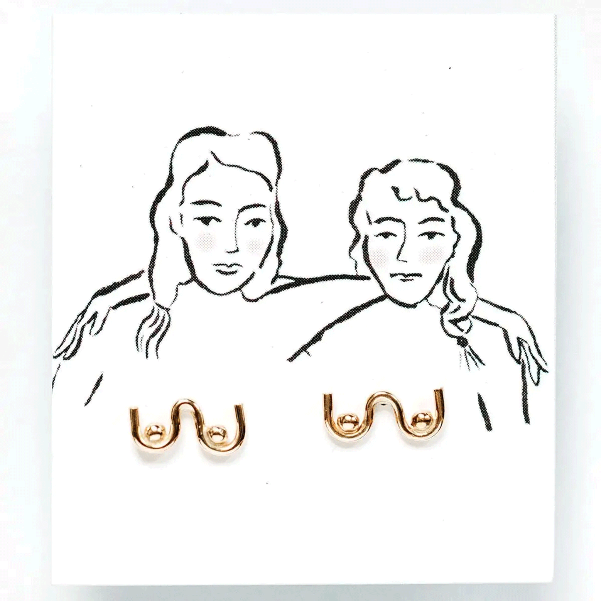On a white background is a gold pair of boob shaped stud earrings on a white card packaging with an illustration of two women.  
