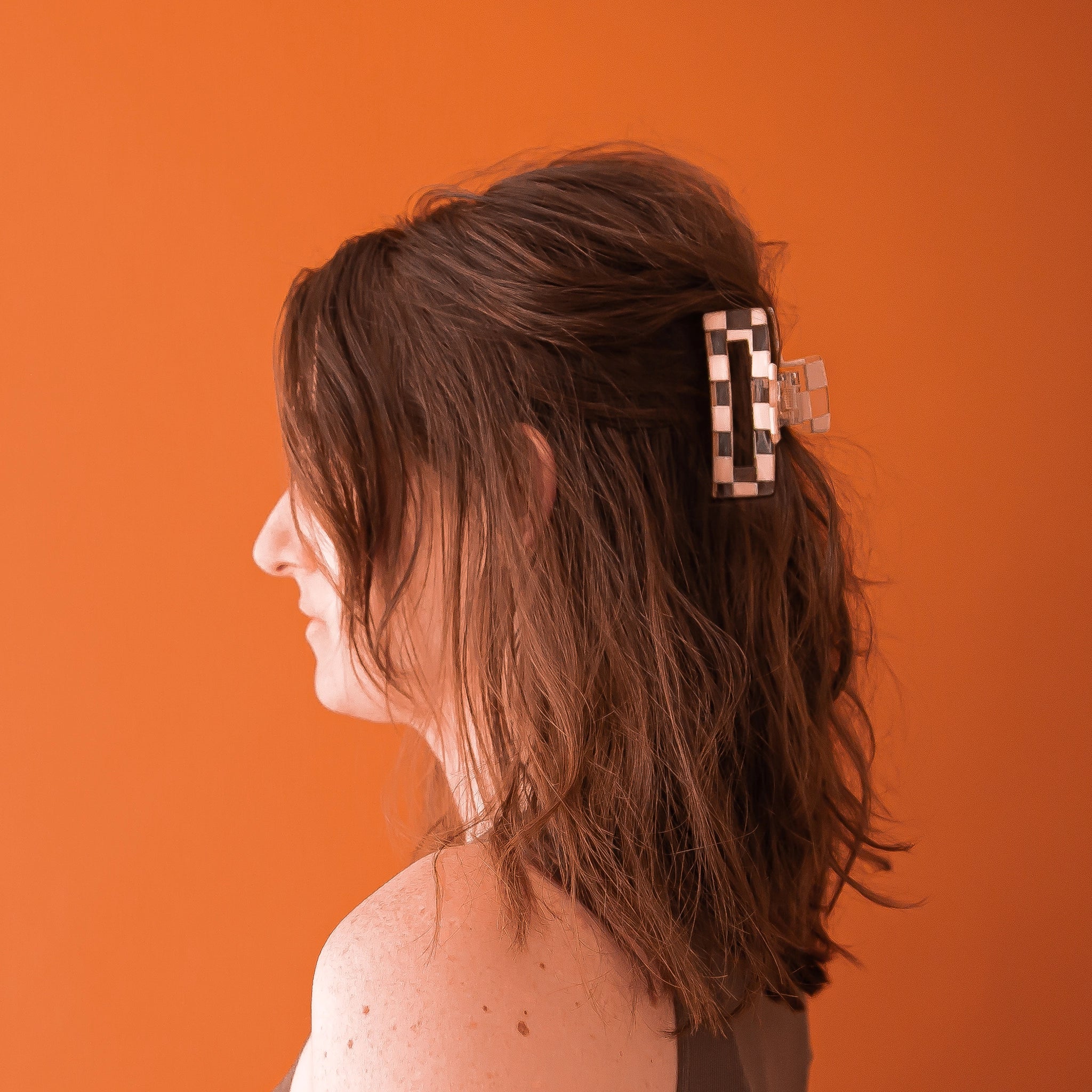 On an orange background is a model wearing the clear and ivory checker claw clip. 