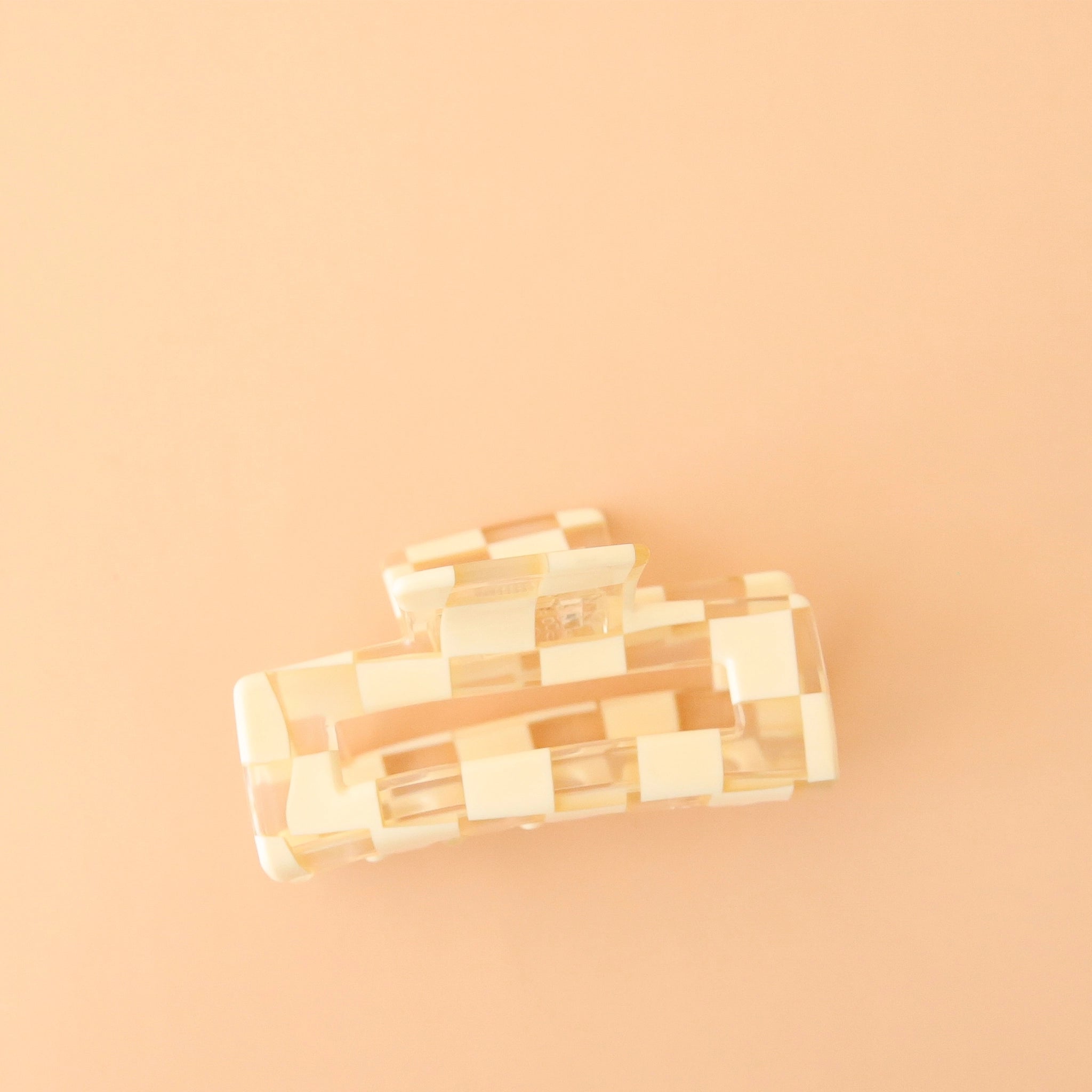 On a peachy background is an ivory and clear checker print claw clip with a rectangle shape.