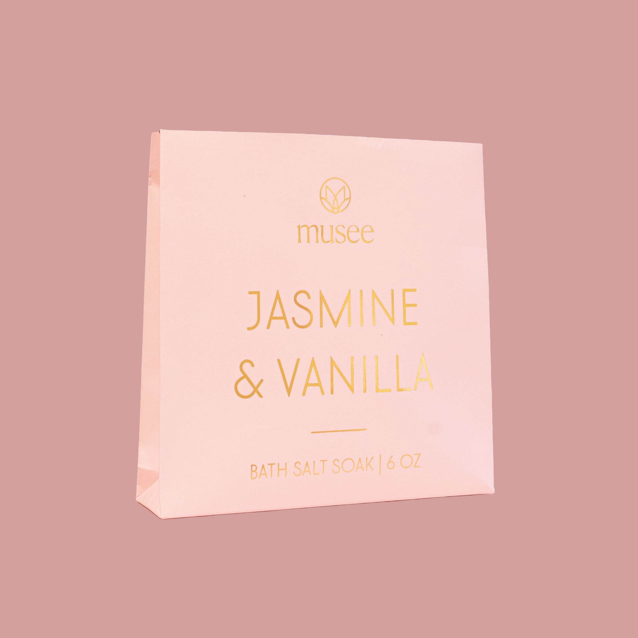 A pale pink package labeled “Musee Jasmine & Vanilla Bath Salt Soak” stands against a muted rose-colored background.