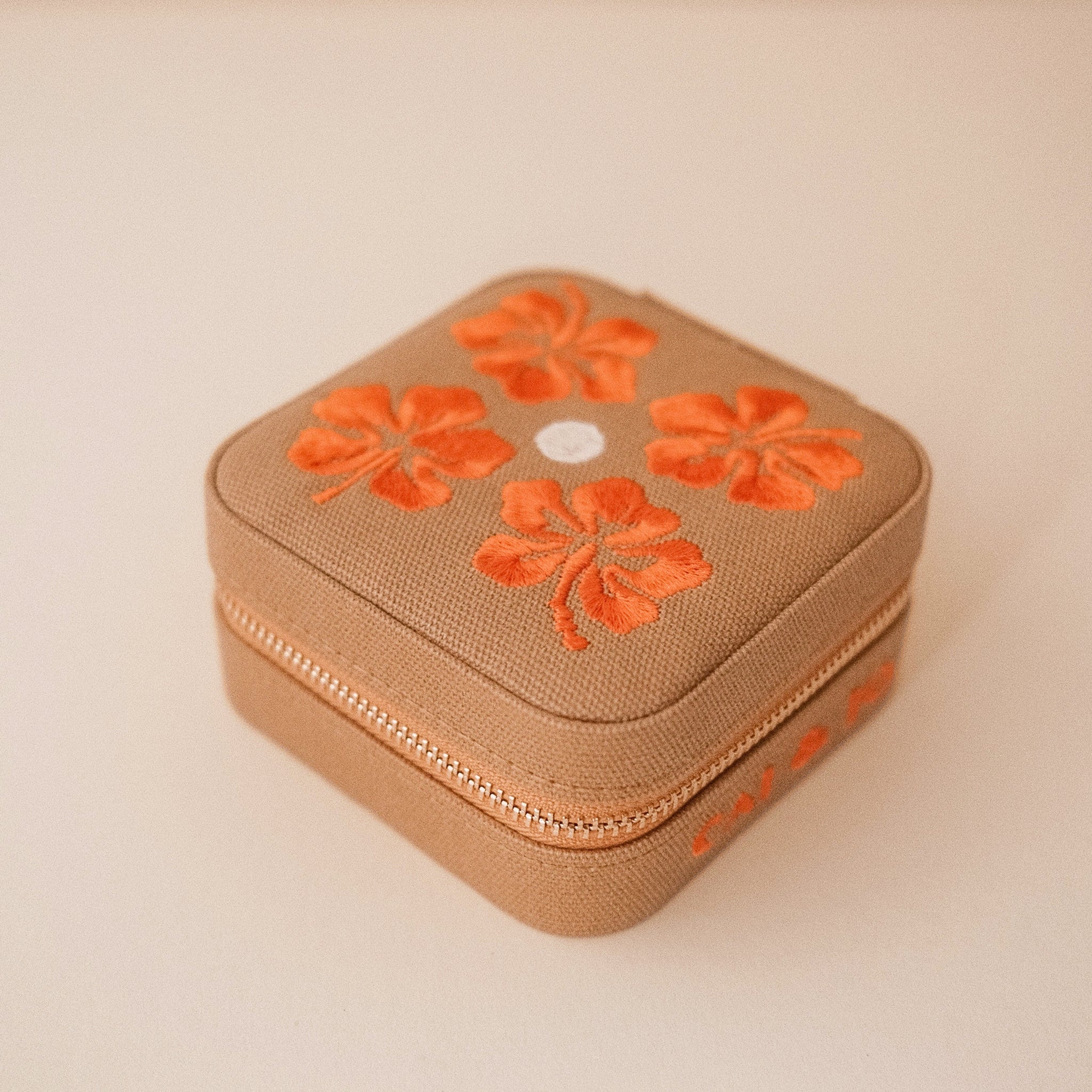 A tan jewelry case with orange flowers. 