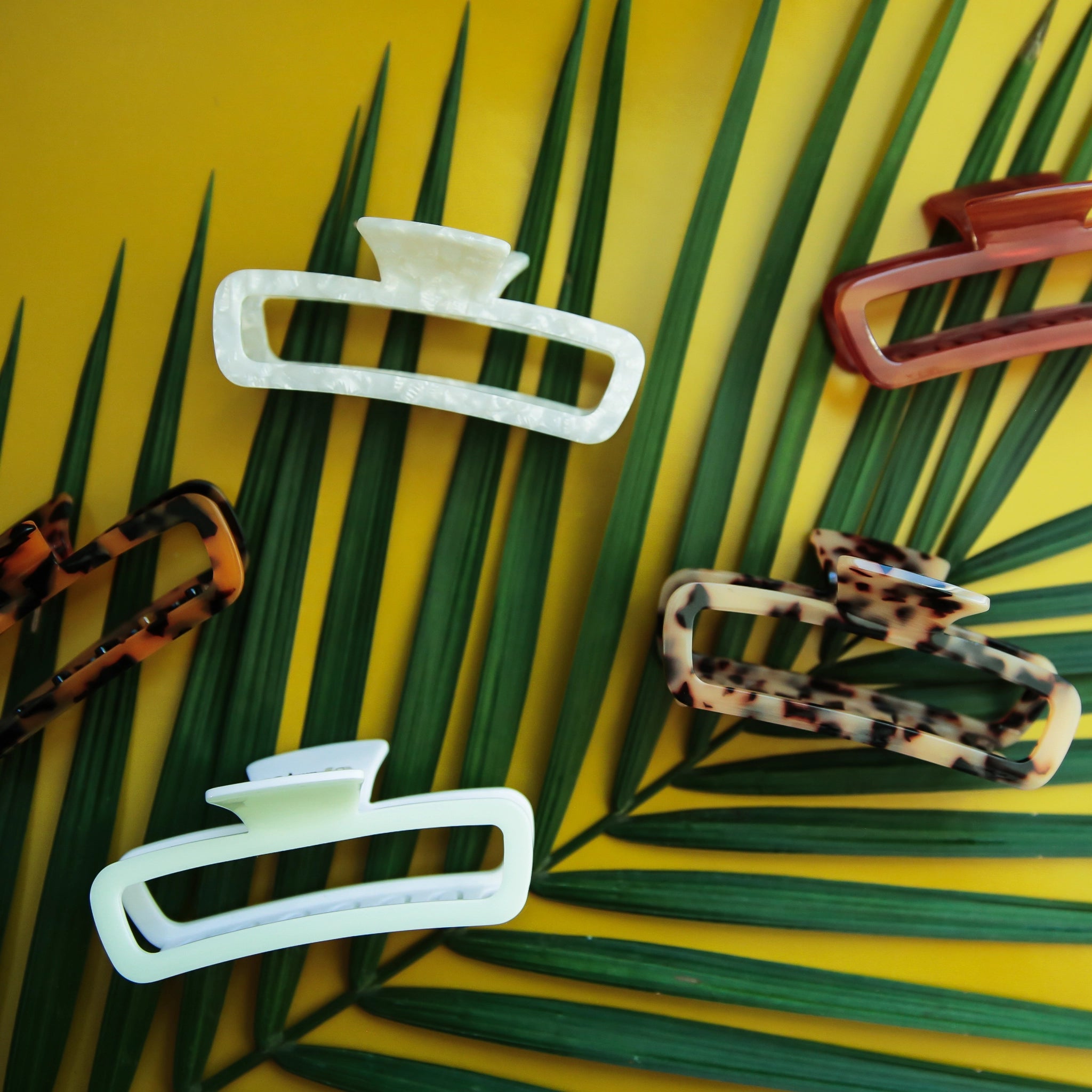On a green background is a variety of rectangle claw clips in tortoise shades, an amber color and two different whites.