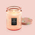 Pink colored embossed candle with patterned colorful lid. The embossed pattern and lid have an abstract floral design with use of the colors peach, gold, and white.