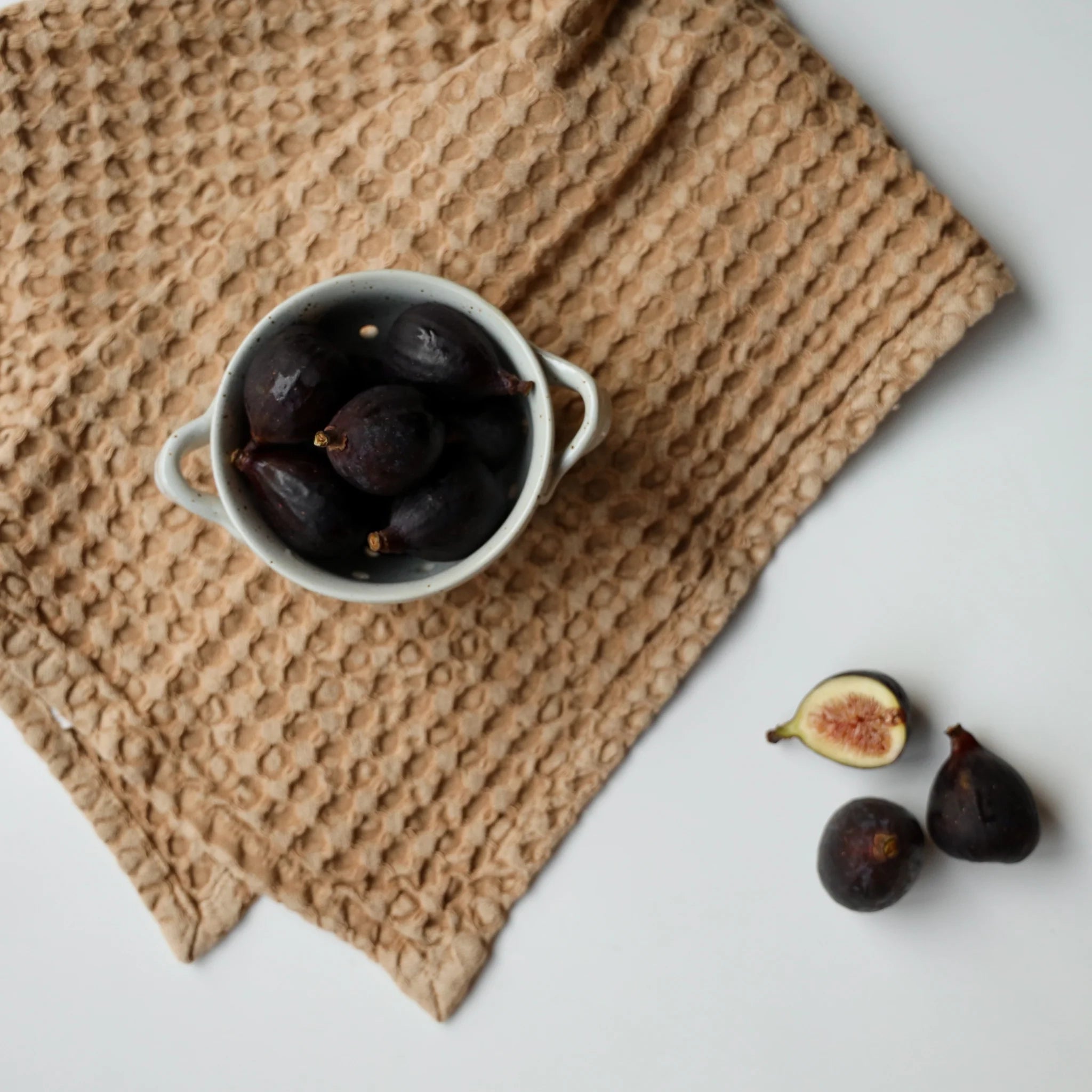 On a white background is a cup of coffee sitting on a waffle knit brown towel. 