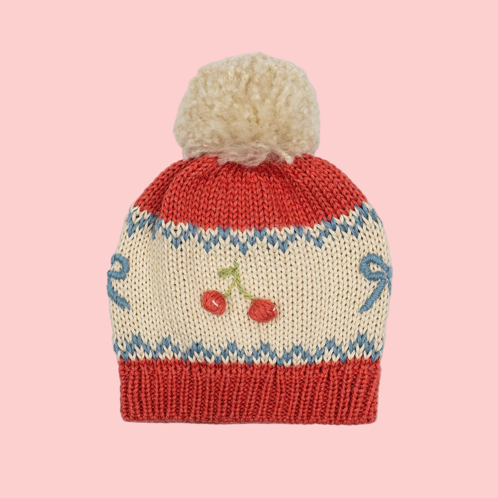 A red white and blue beanie with a puff top and a cherry and bow design. 