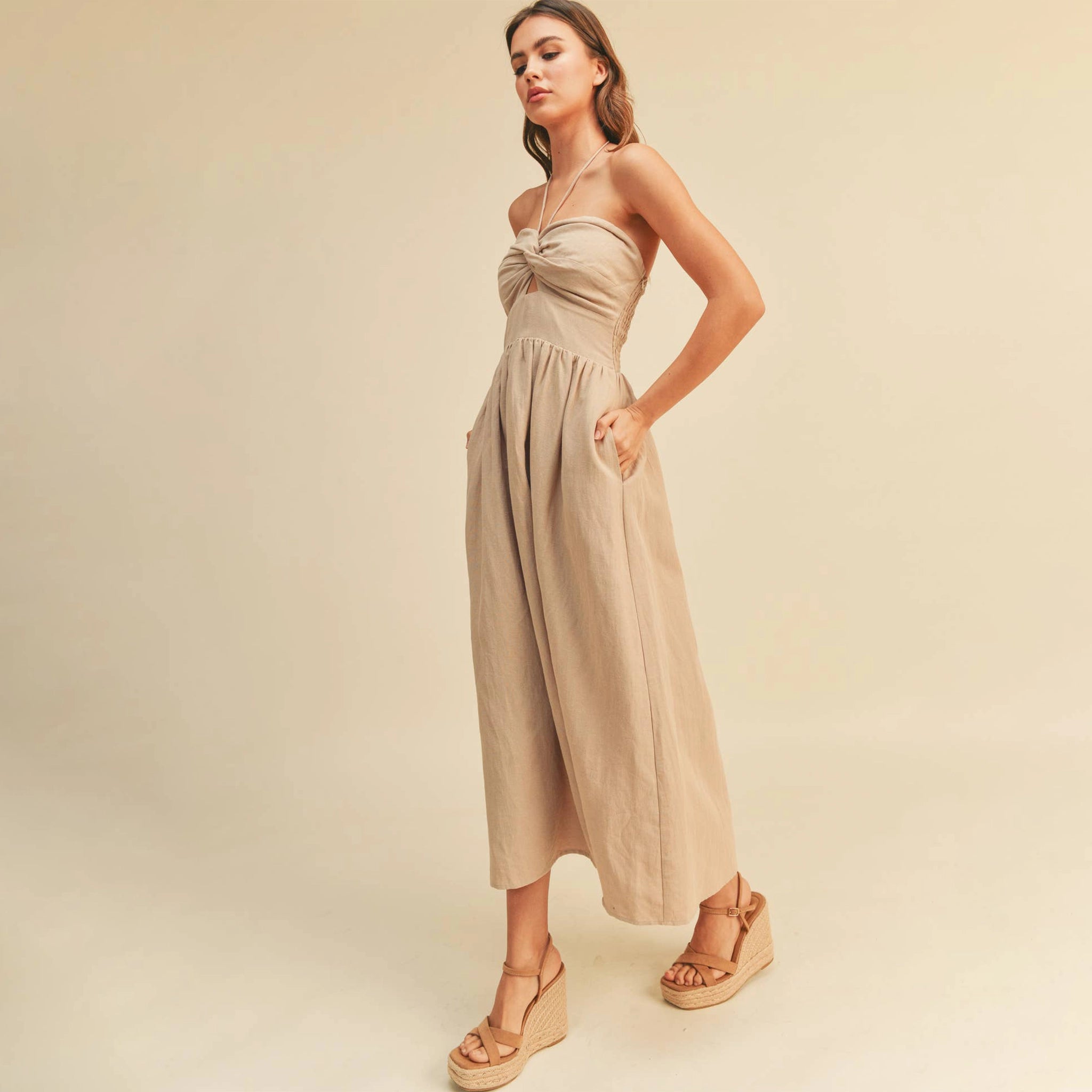 On a tan background is a model wearing the neutral Knotted Front Halter Neck Dress in the shade stone.