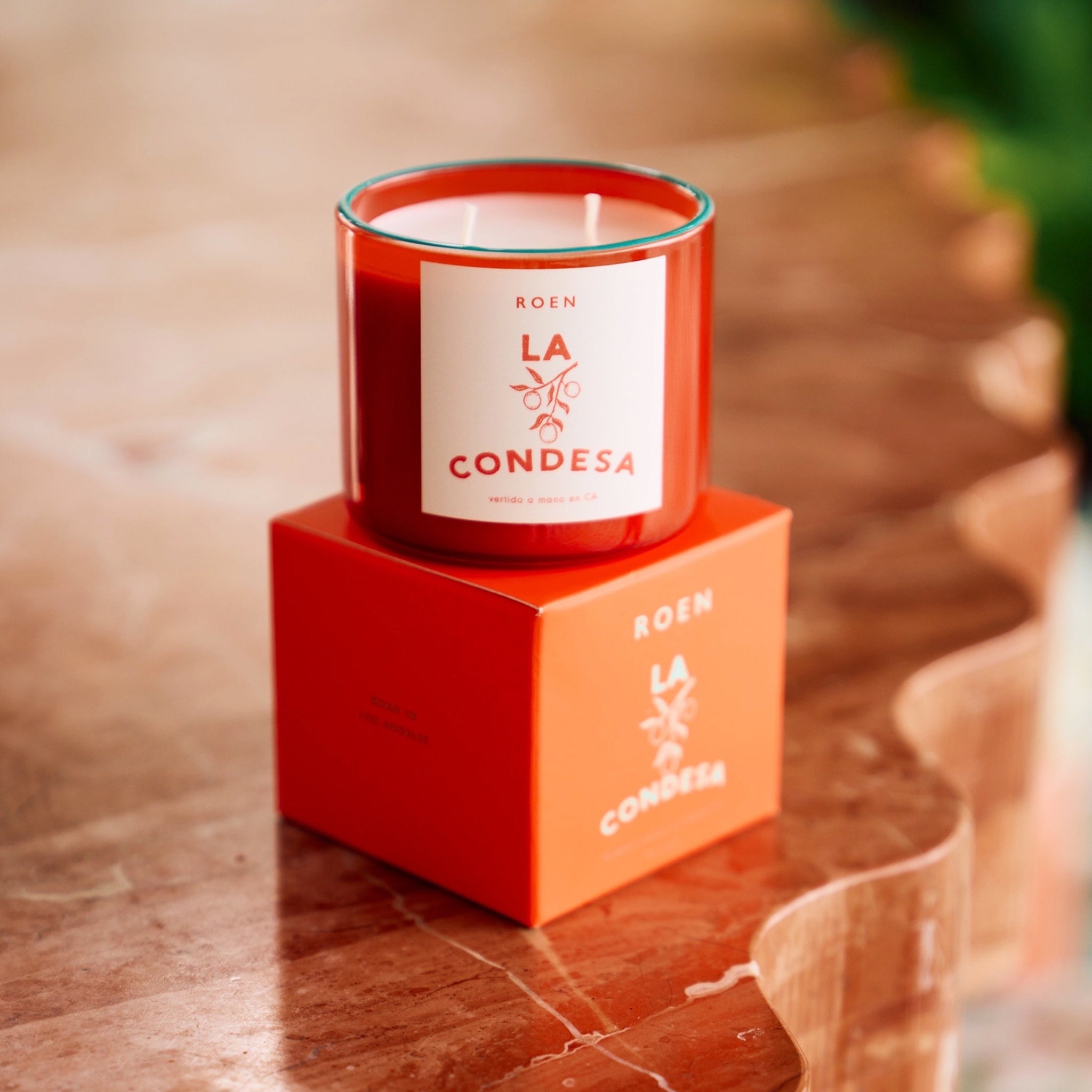 An orange/red glass jar candle with a label that reads, "La Condesa".