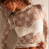 Woman wearing a sheer lace top with long sleeves against a neutral background