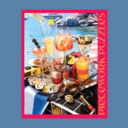 A hot pink puzzle box with an image of a beachside drinks tray with a variety of cocktails and beachside essentials. 
