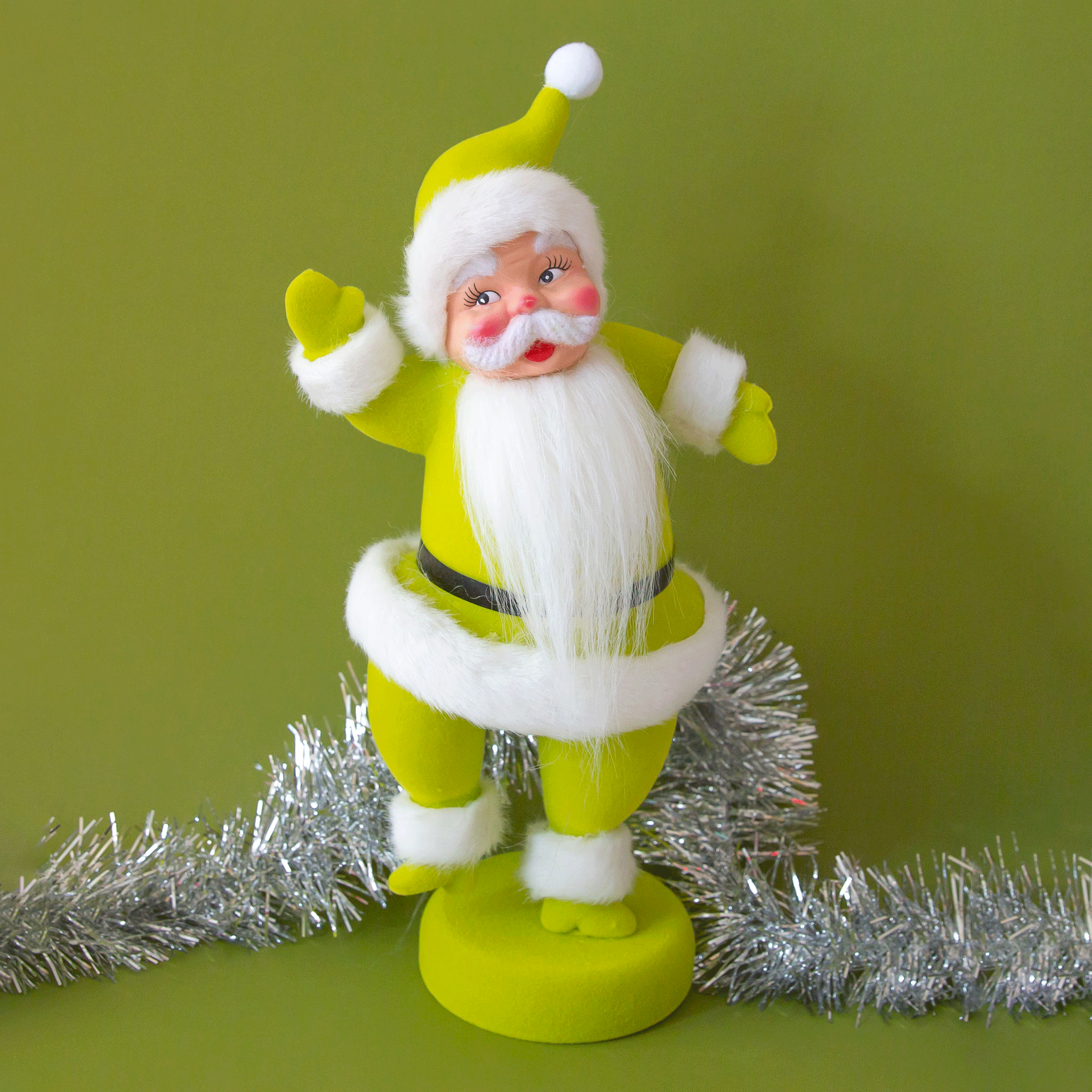 A plastic santa figurine with a chartreuse suit on with furry detailing the cuffs, jacket and hat.