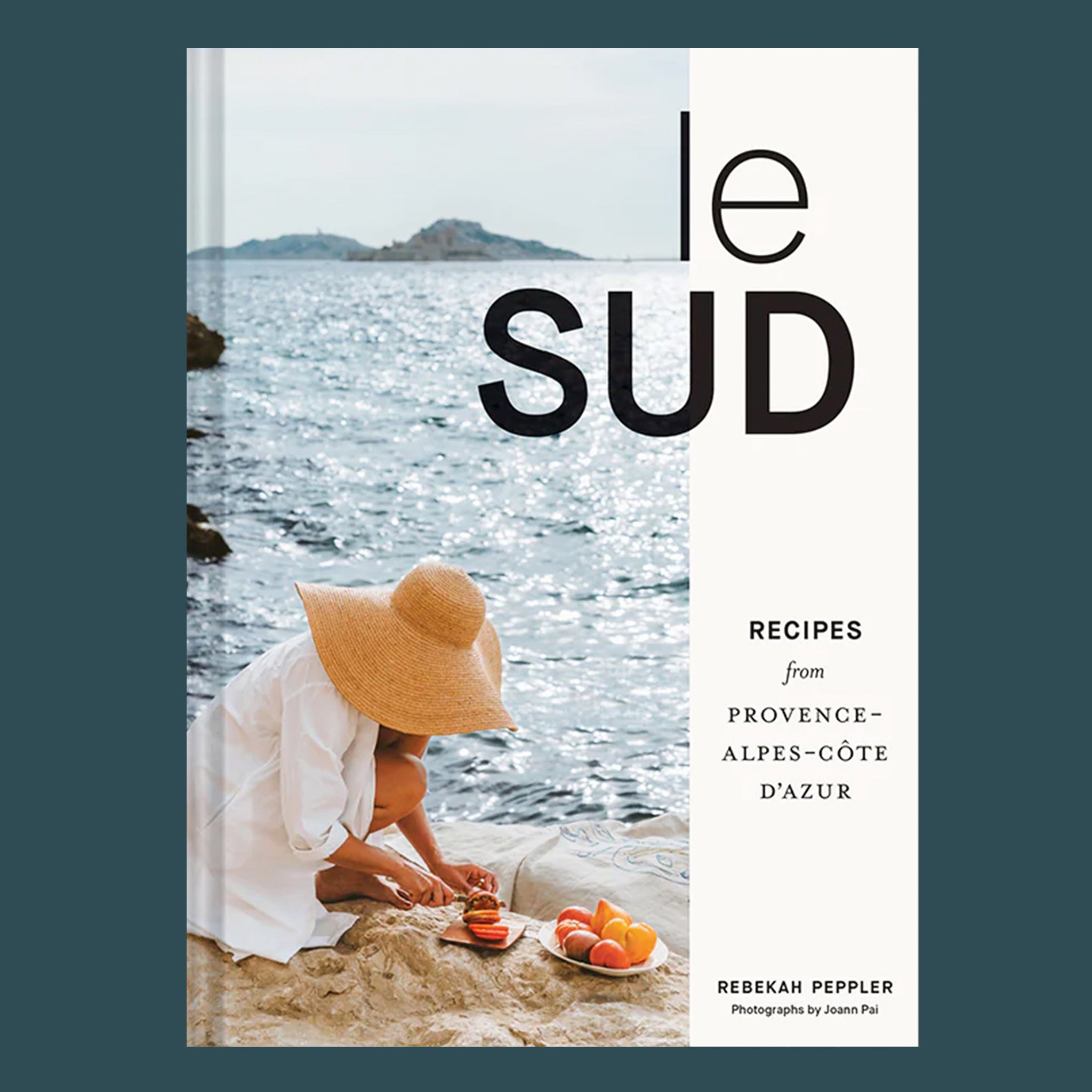 A book cover with a photo of someone cutting fruit on rocks next to the ocean and black text that reads, 'le sud Recipes from Province Alpes-Cote Dazur'. 