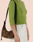A leopard print curved crescent shaped handbag with a black strap that can adjust from a shoulder bag length to a crossbody. 