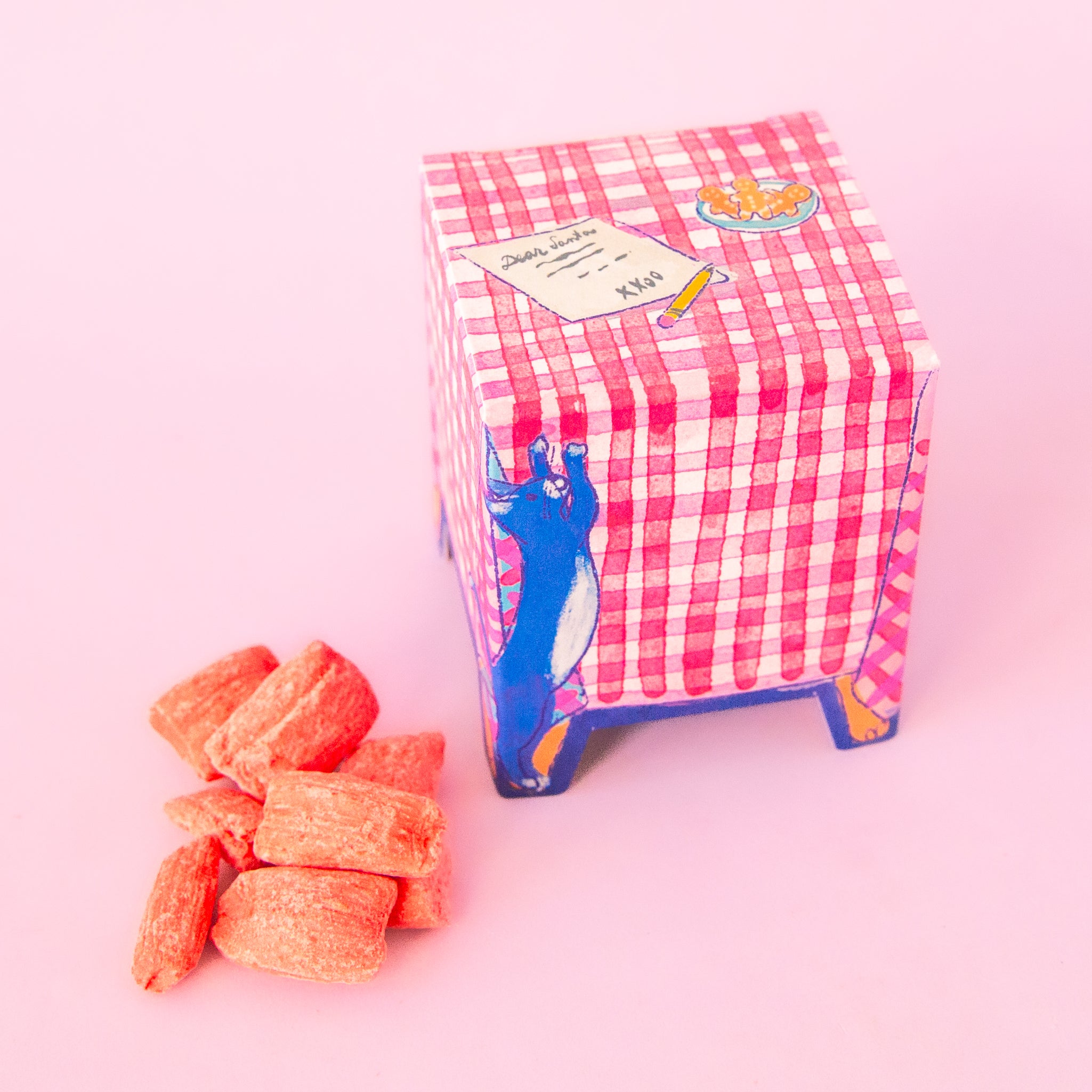 A box of candies with packaging in the shape of a table with a cat scratching at the table cloth and a letter to santa on top, 