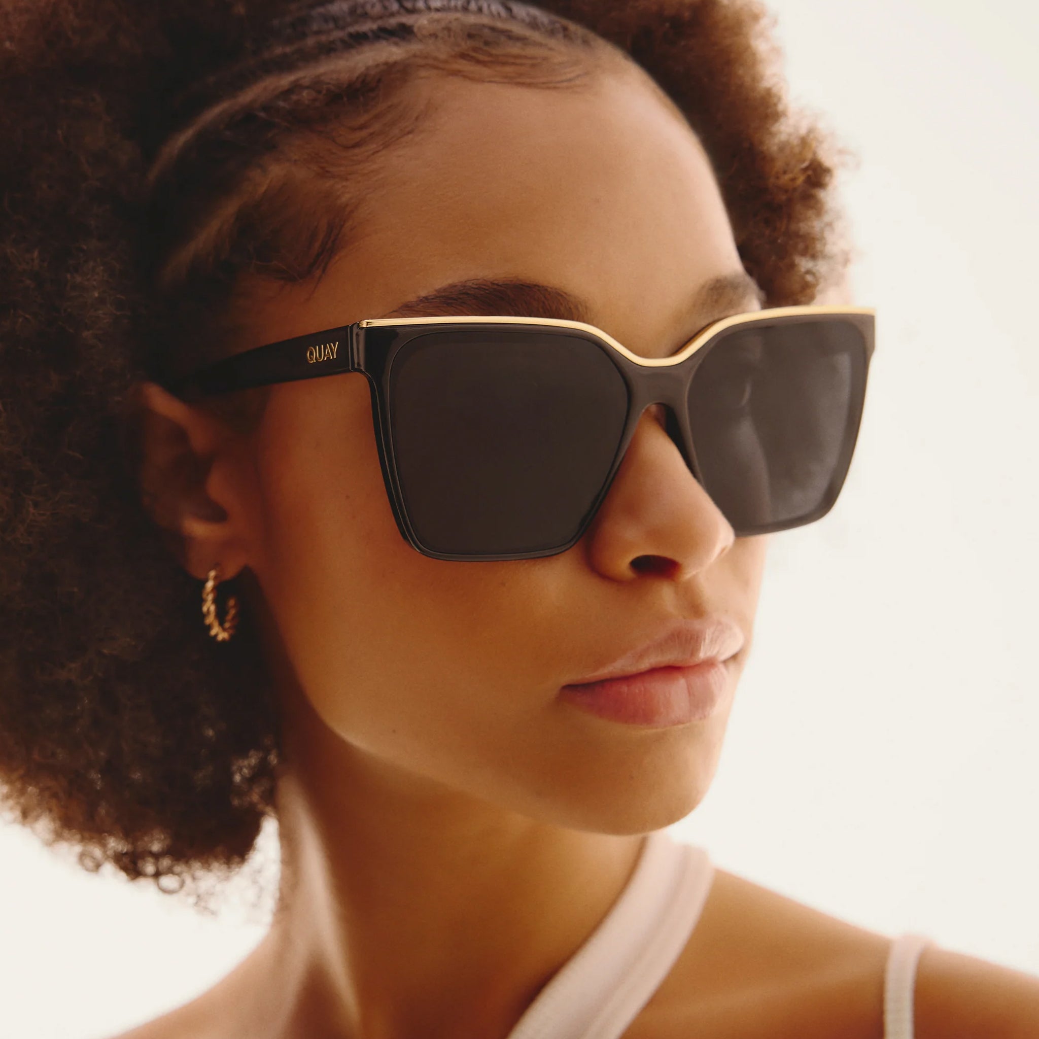 A black pair of oversized square sunglasses with a gold lined top. 