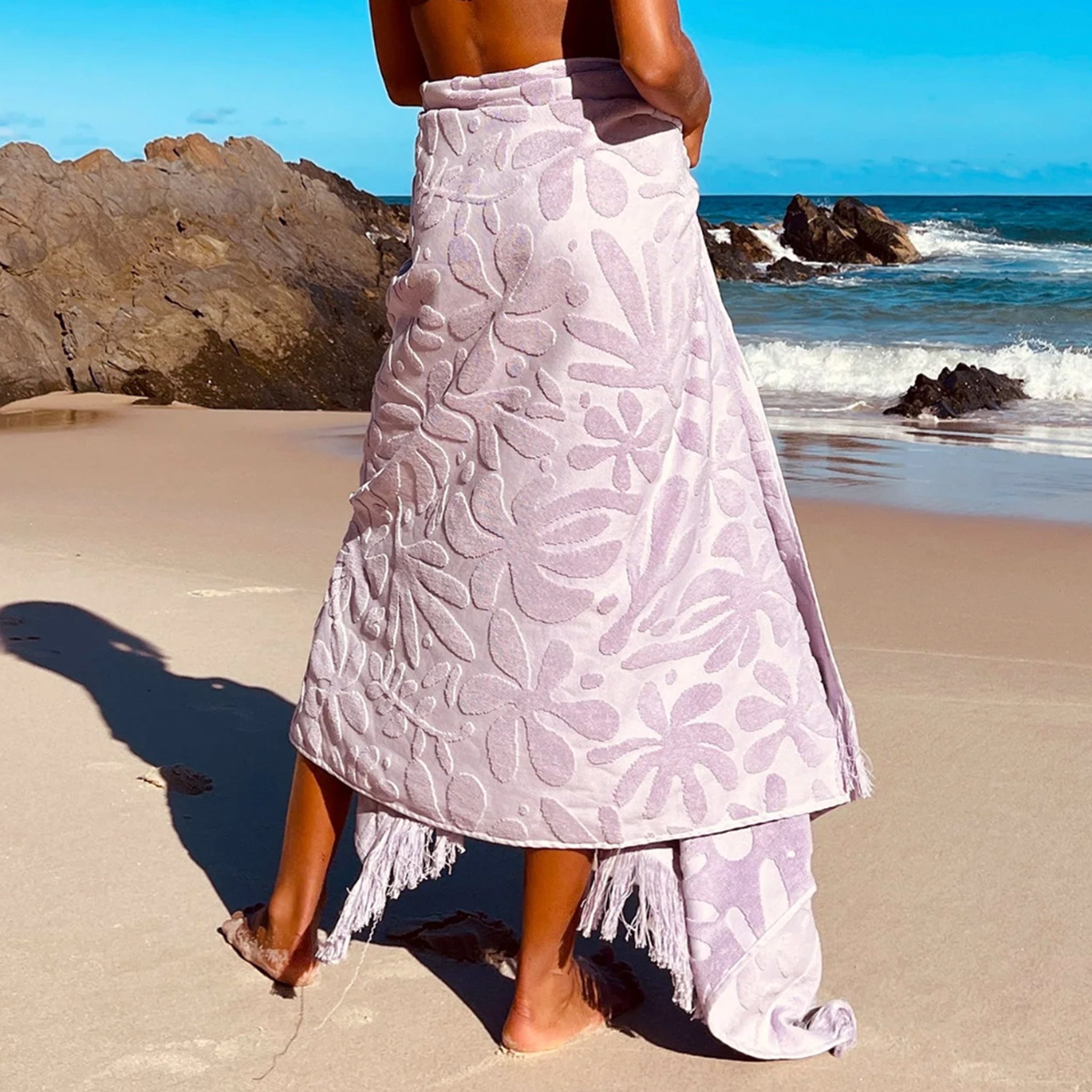 A light purple towel with a subtle floral print and fringe edge