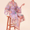 A woman sitting on a stool modelinga lilac robe with a floral and tiger design.