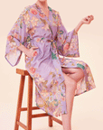 A woman sitting on a stool modelinga lilac robe with a floral and tiger design.