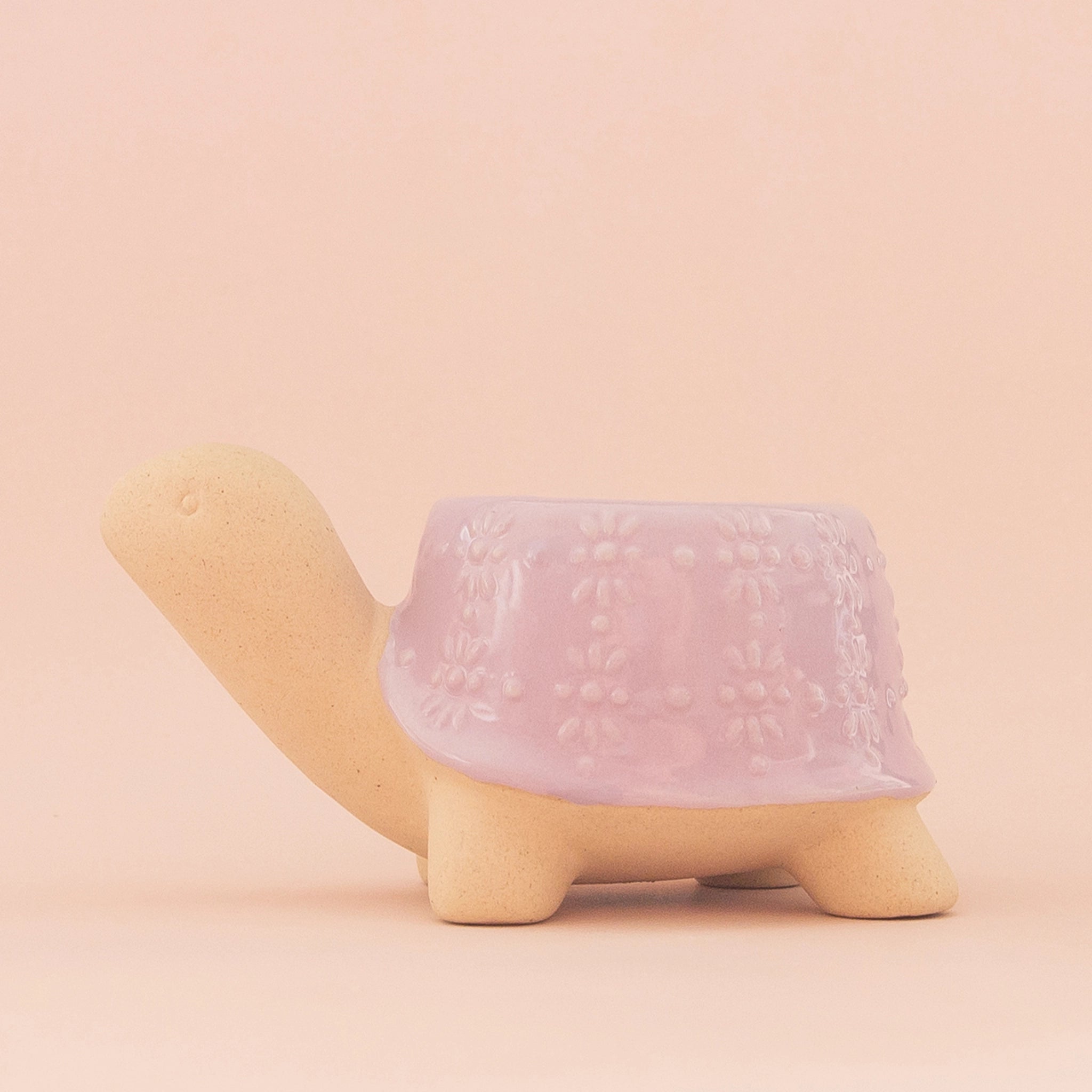 On a peachy background is lilac ceramic turtle shaped planter.