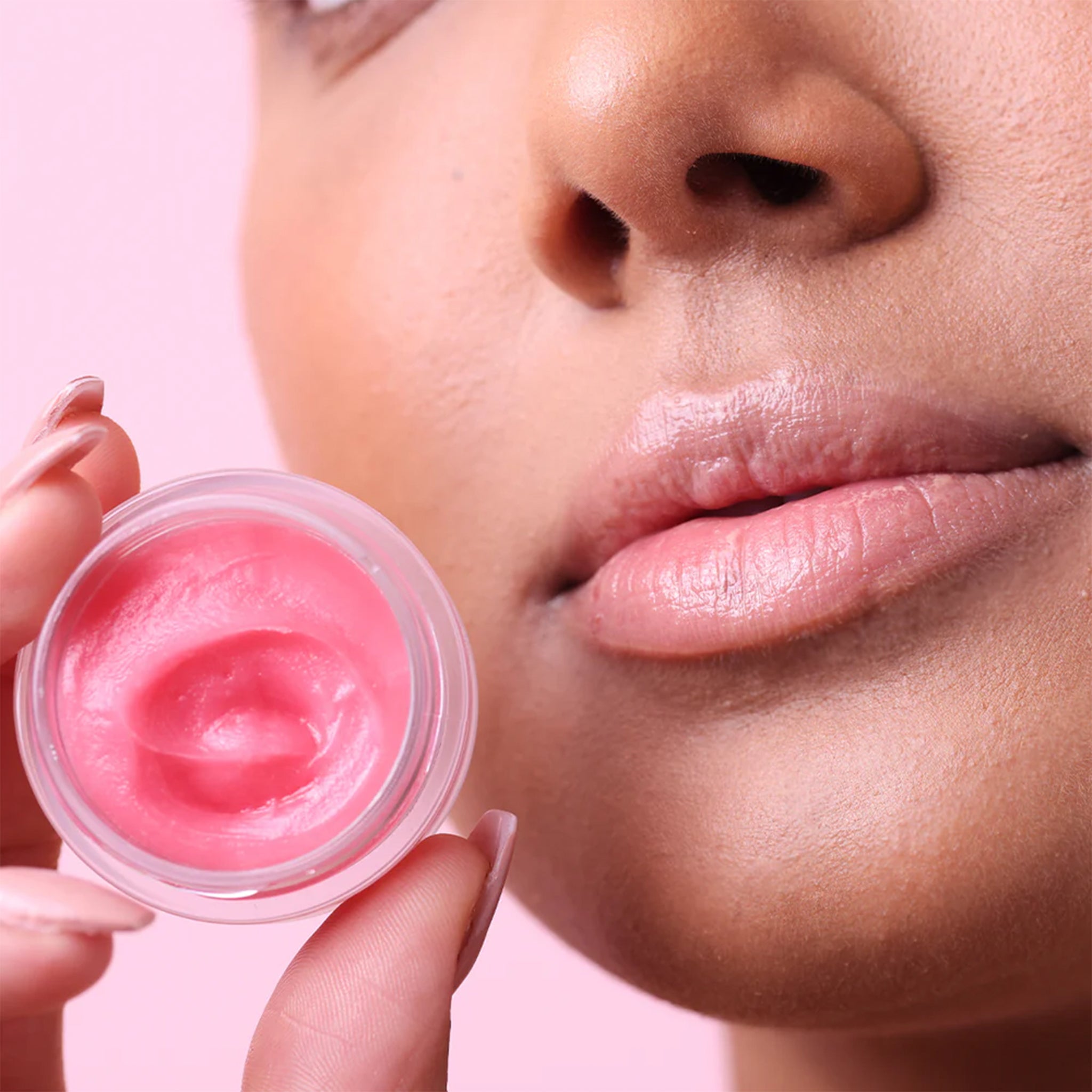 A model holding a small jar of pink lip balm. 