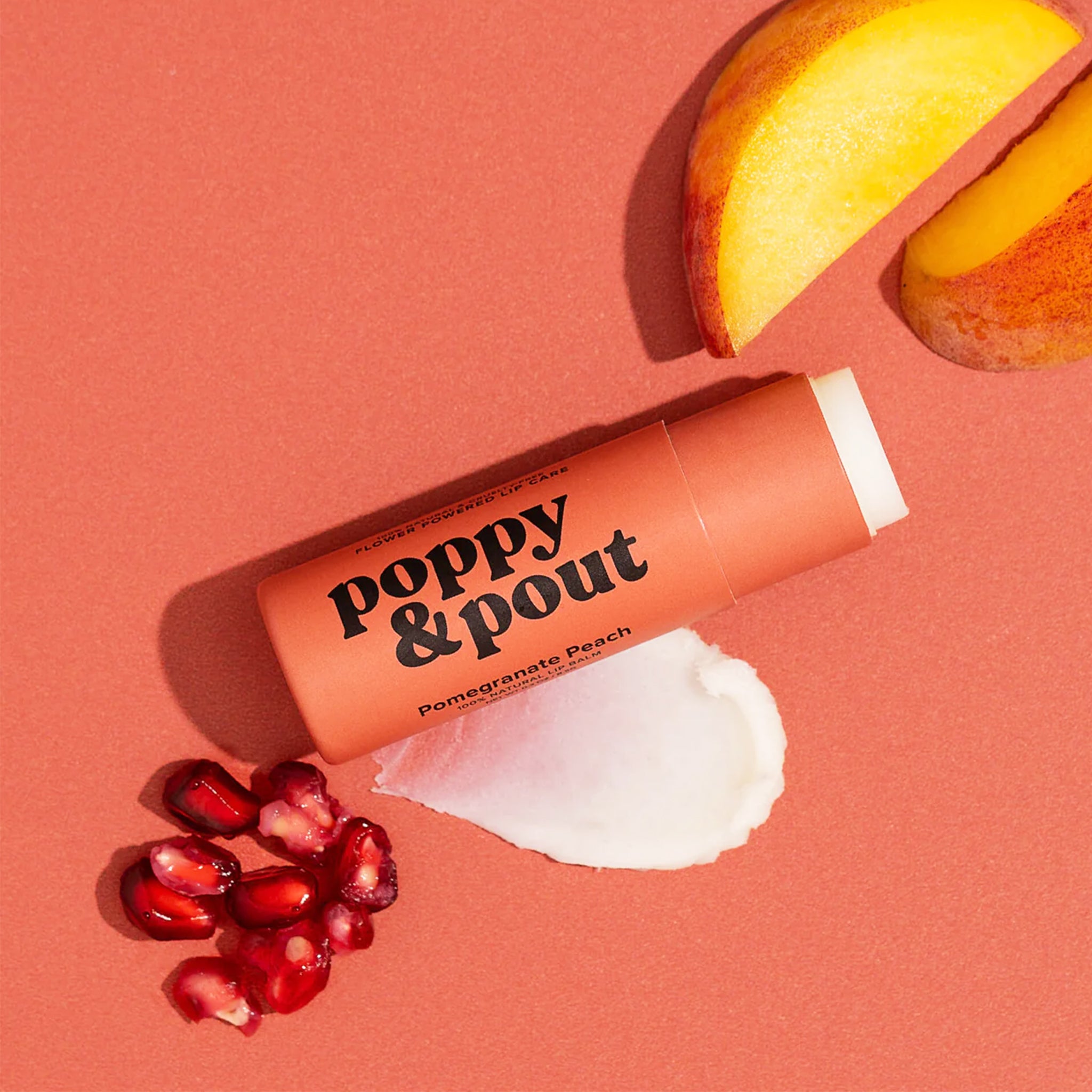 A peachy colored tube of lip balm with black text that reads, "poppu & pout pomegranate peach". 