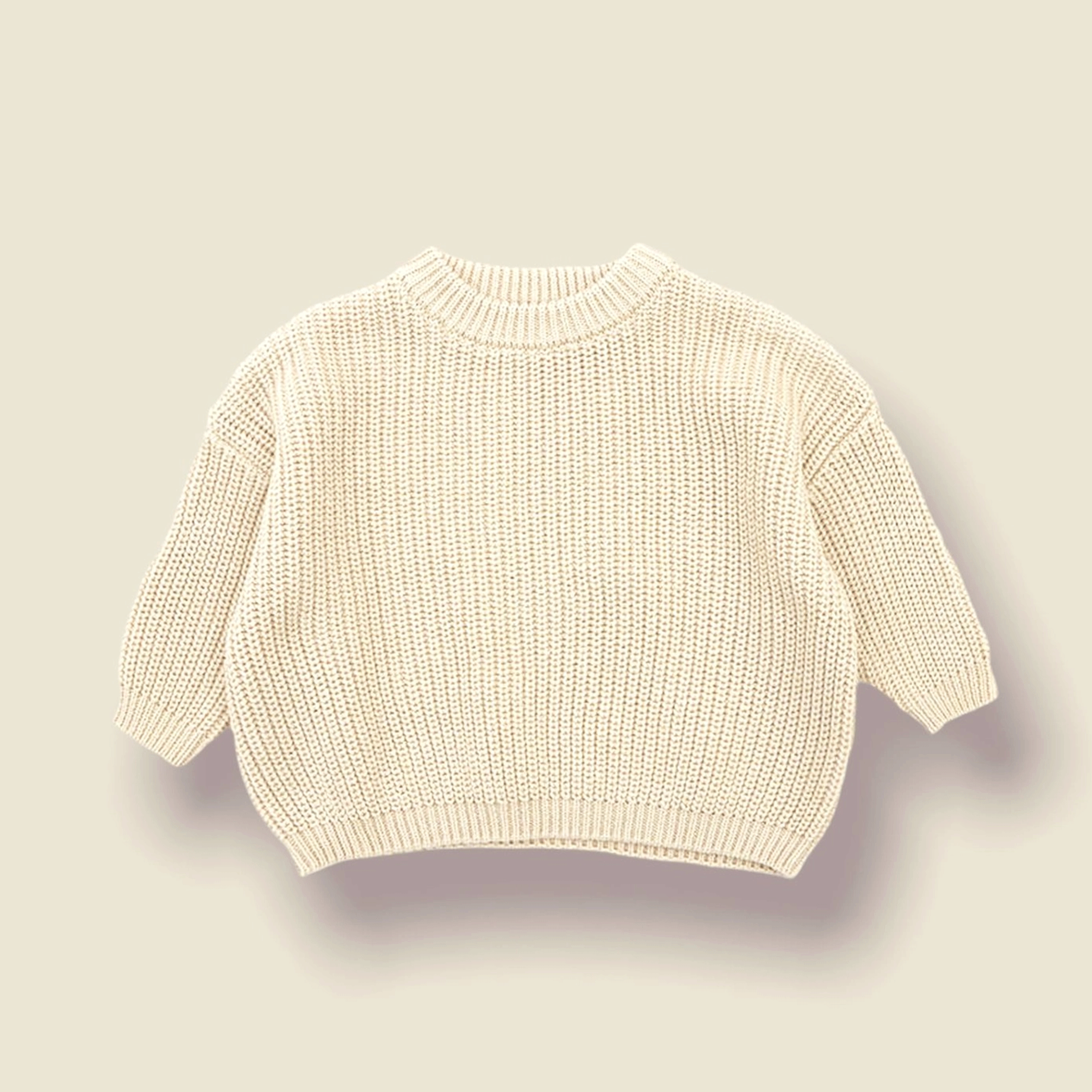 On a neutral background is an ivory knit sweater for children. 