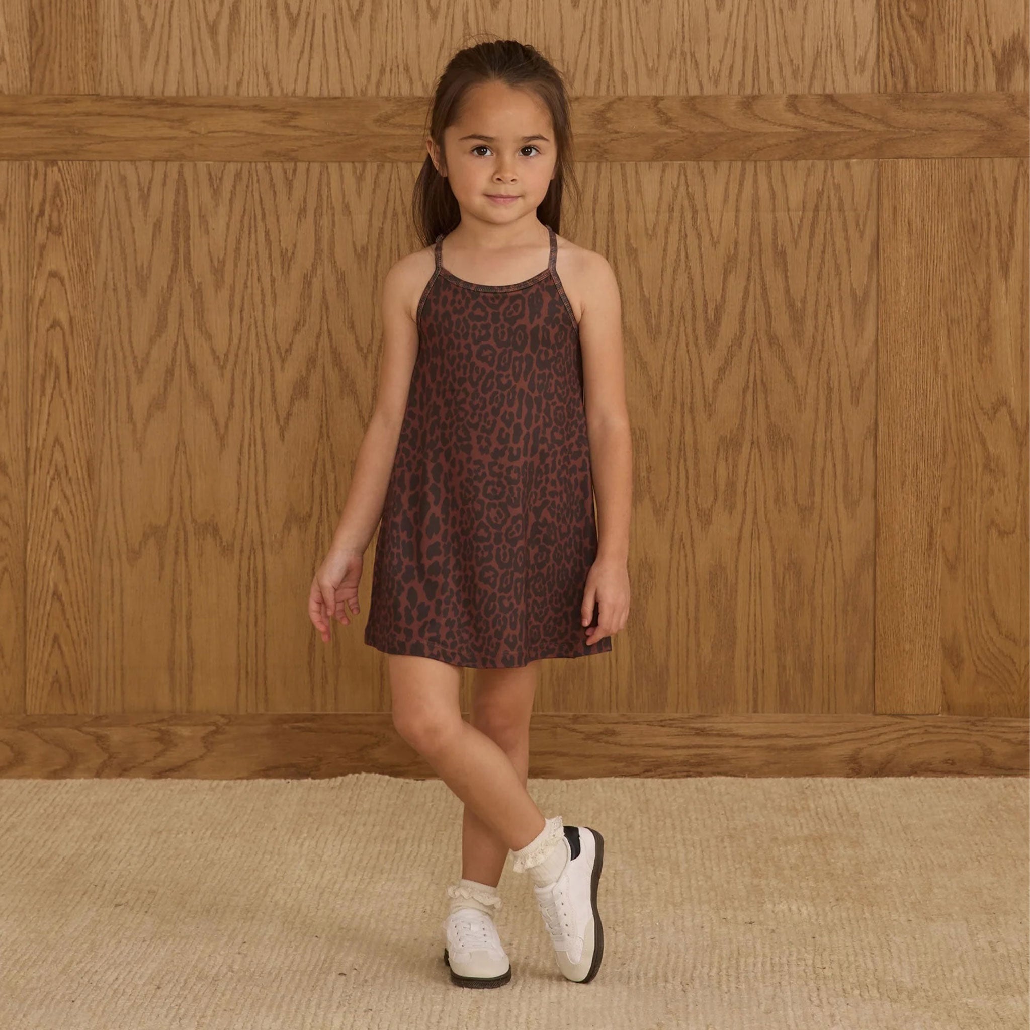 Little girl wearing a black and brown leopard print dress with thin straps. 