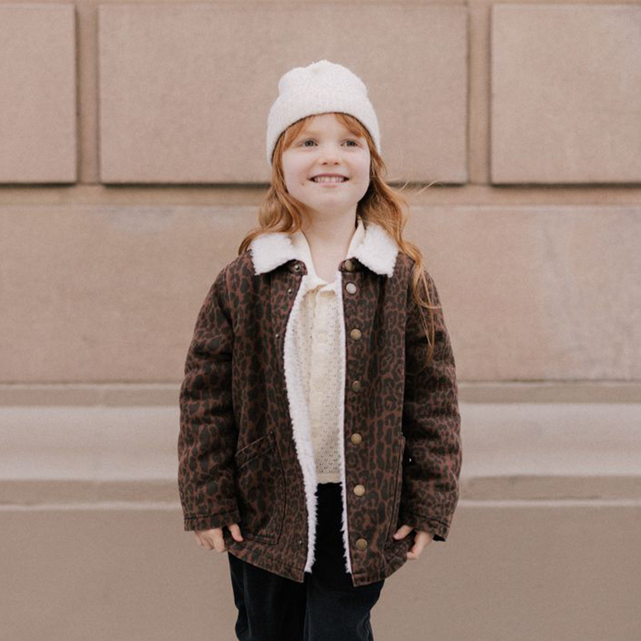 A children's brown leopard print jacket with a cream colored boucle interior and collar. 