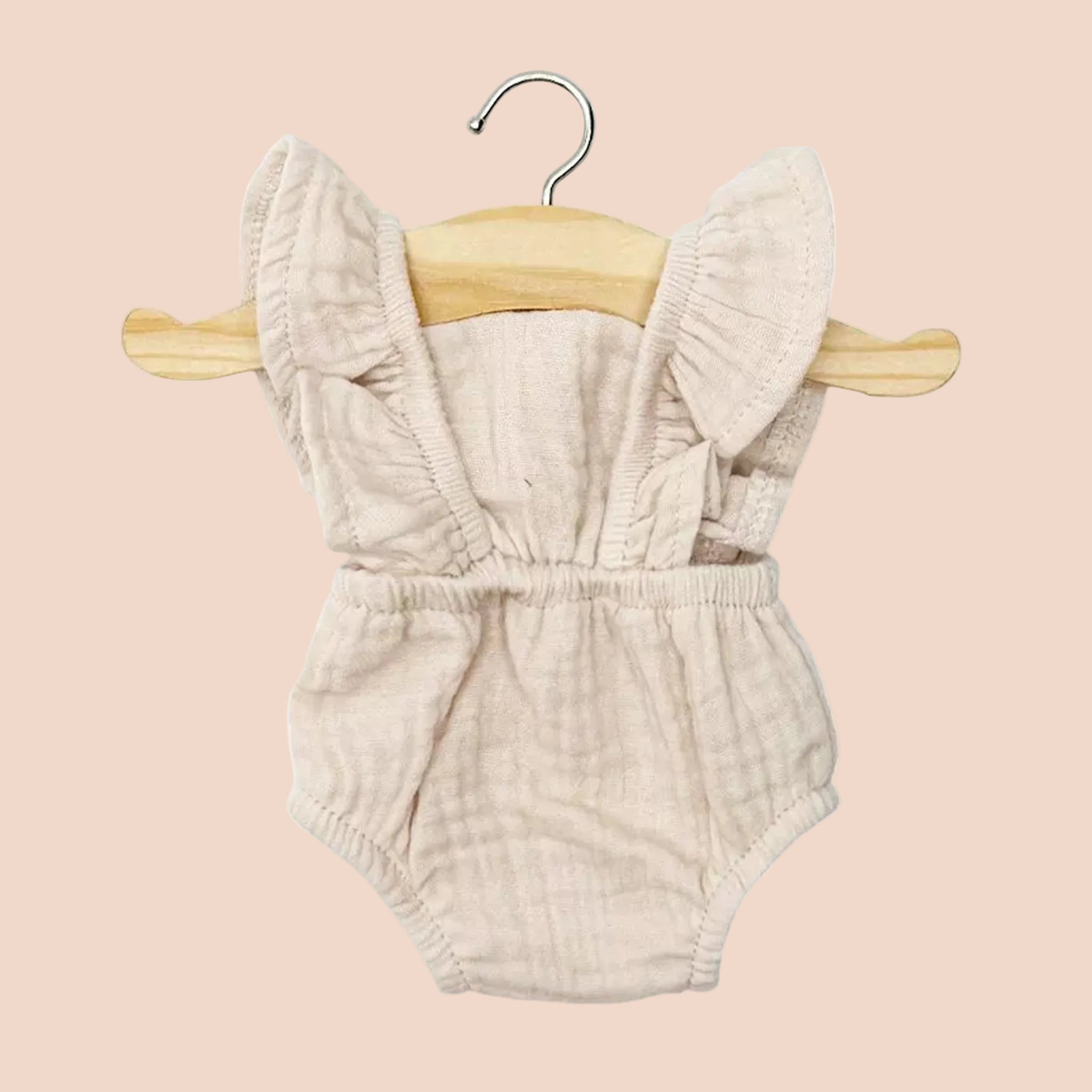 Beige baby doll romper with ruffled details on a wooden hanger against a white background